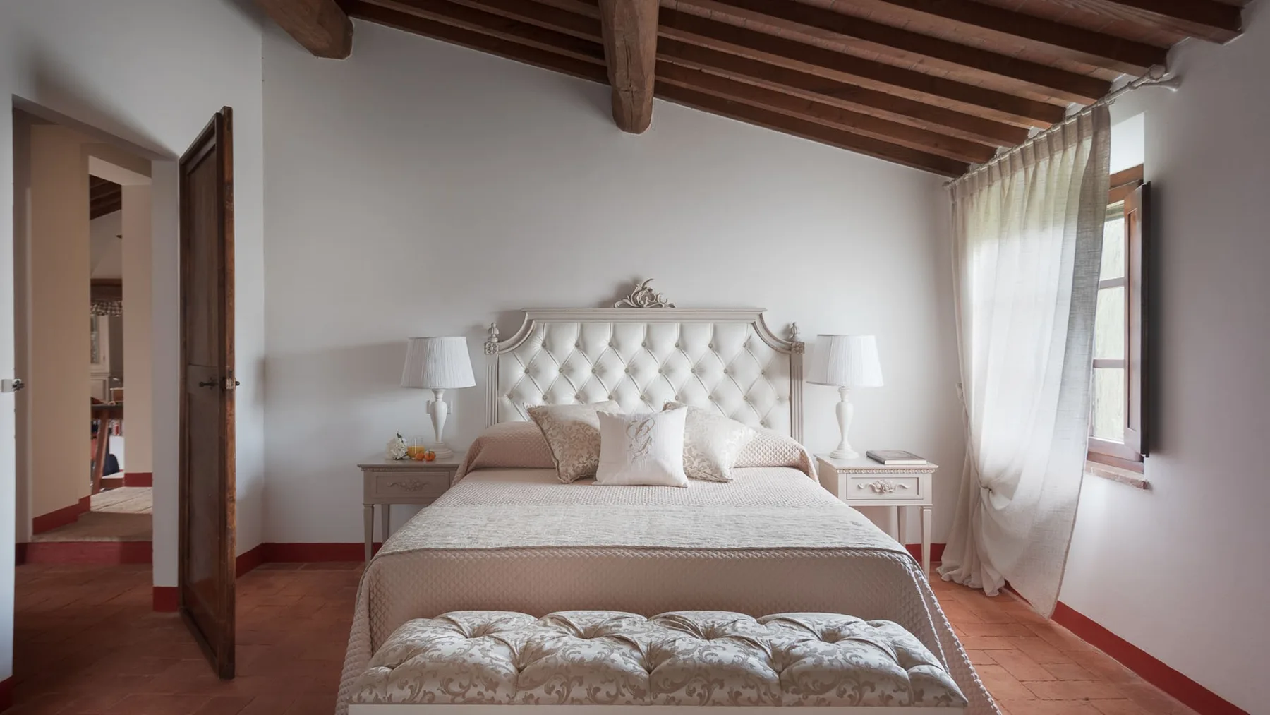 Un dormitorio con una cama, mesillas a juego y una ventana con cortinas translúcidas.