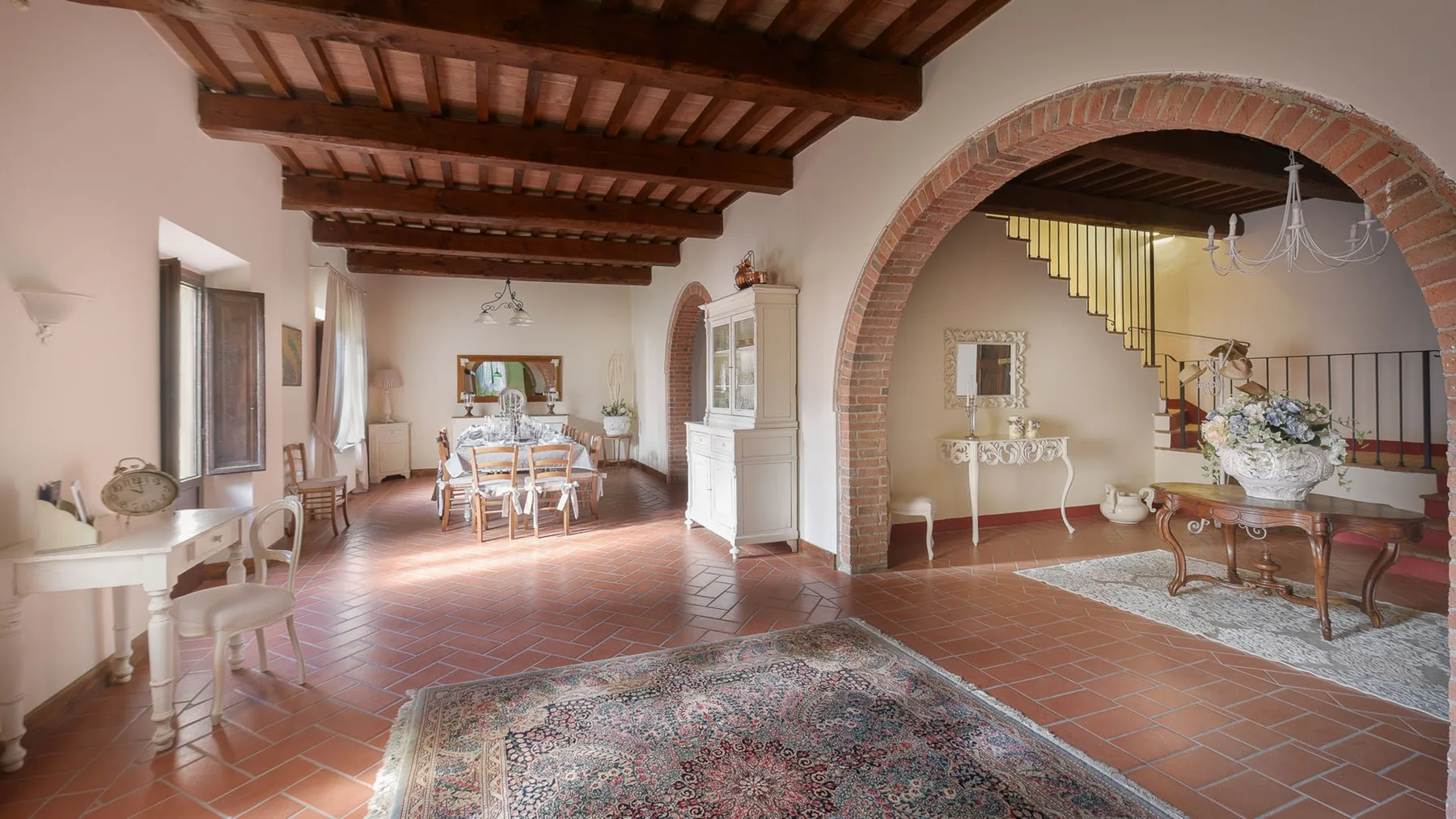 Un amplio salón comedor con suelo de terracota y techo de madera vista.