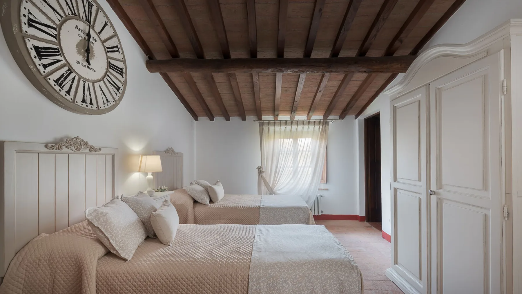 Un dormitorio con dos camas, armarios blancos con paneles y vigas de madera expuestas en el techo.