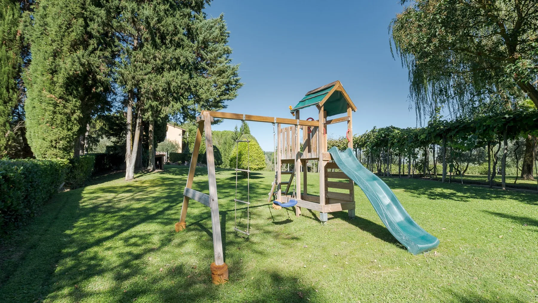 Un parque infantil de madera con tobogán y columpios está en un césped.