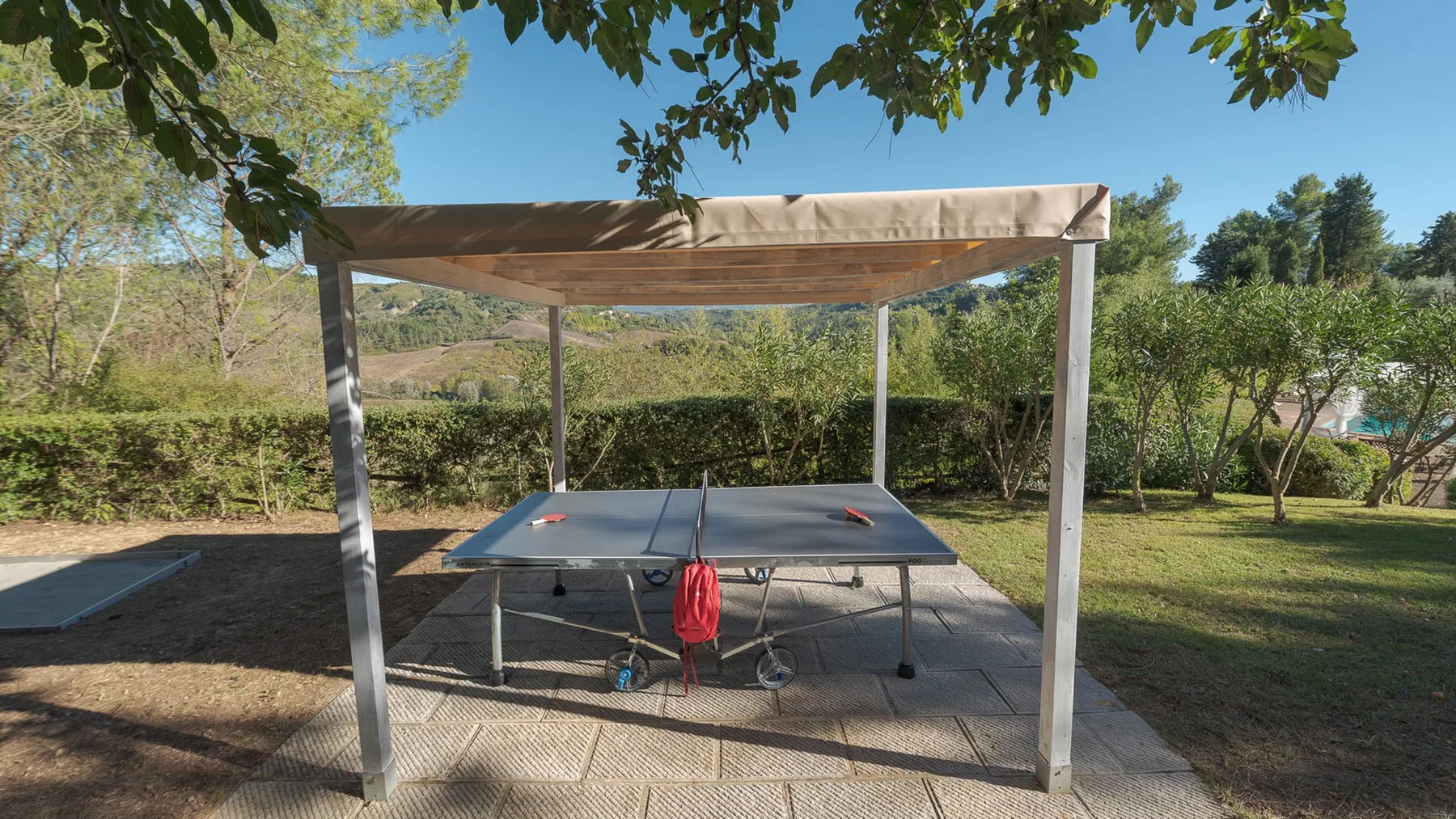Una mesa de ping-pong al aire libre está bajo un toldo en un jardín.