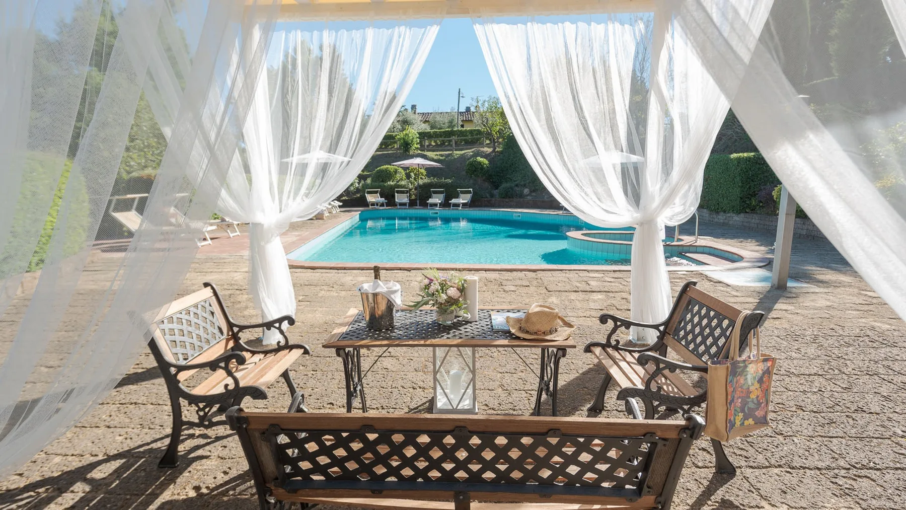 Una zona de asientos al aire libre, bajo cortinas translúcidas, da a una piscina.