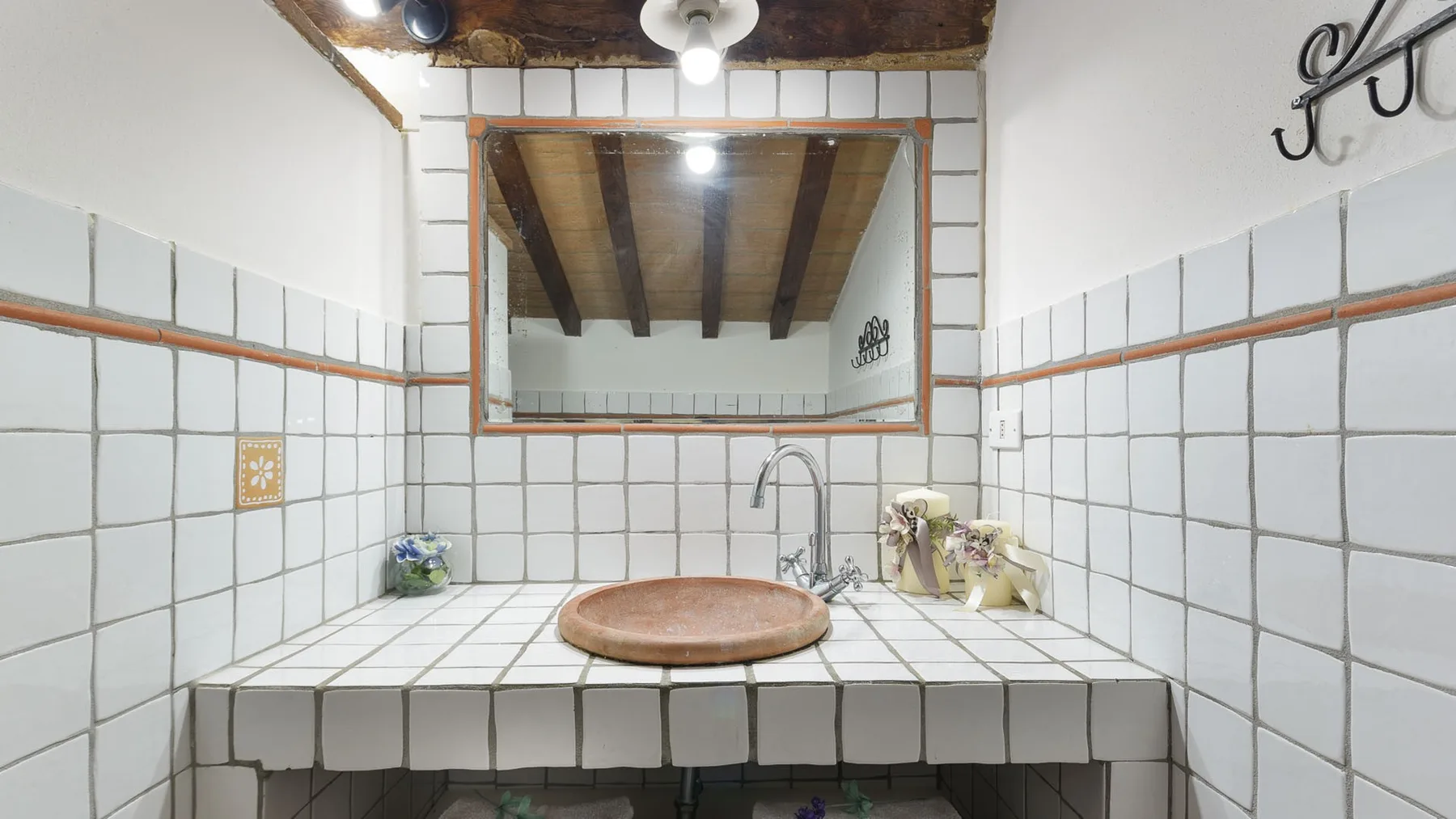 Un lavabo de baño revestido de azulejos, con una pila redonda, grifo y espejo grande.