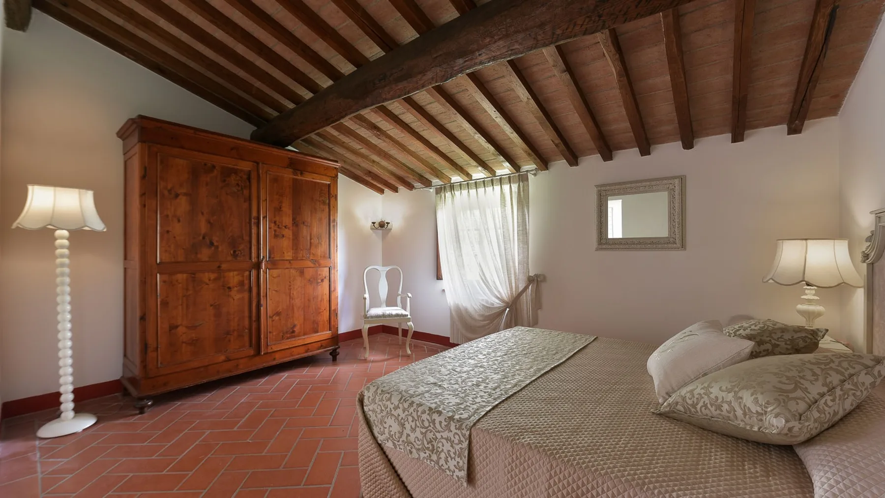 Un dormitorio con un gran armario de madera, ropa de cama estampada y vigas expuestas en el techo.