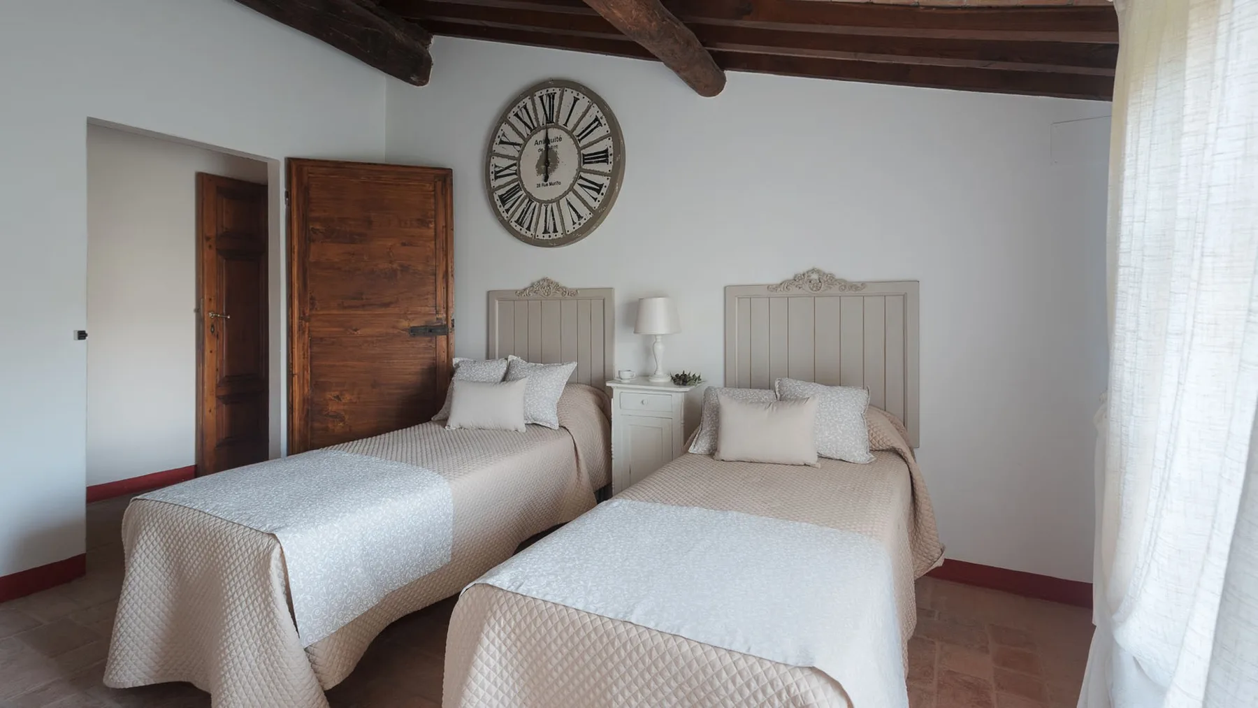 Un dormitorio con dos camas bien tendidas bajo un gran reloj de pared.