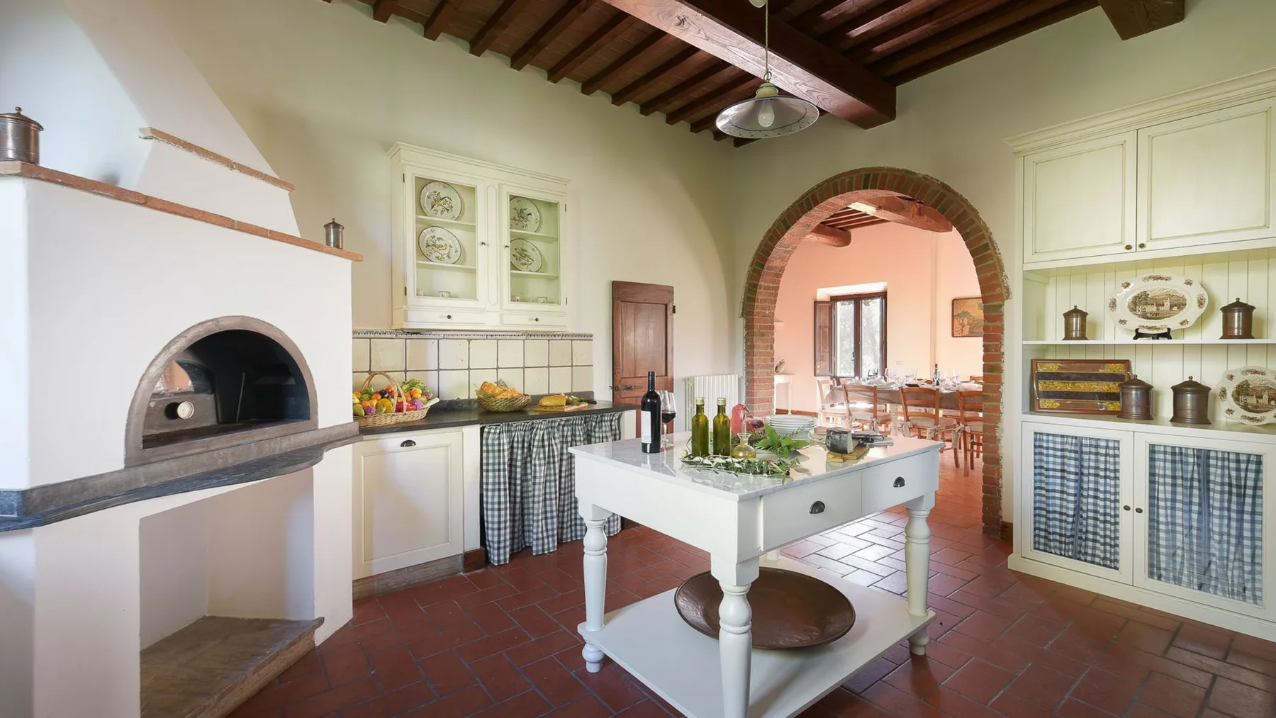 Una cocina rústica con una isla central, suelo de baldosas y un arco.