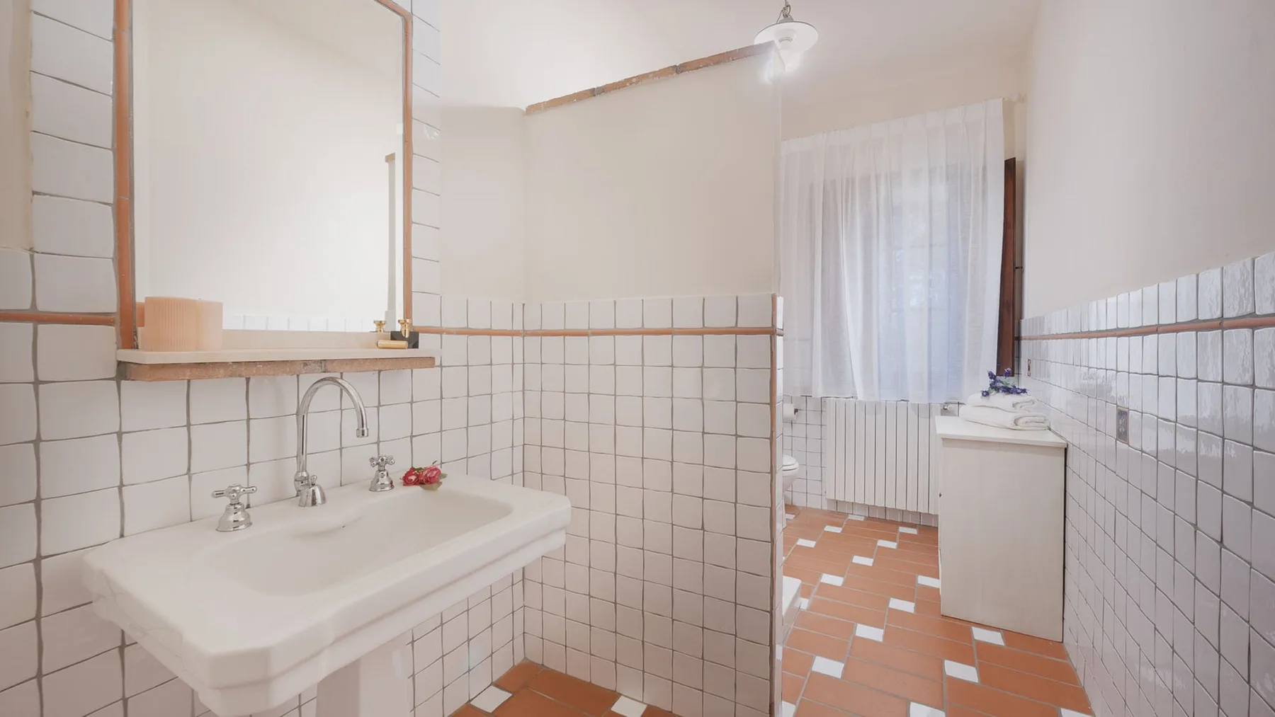 Un baño alicatado con un lavabo y una ventana con cortina.