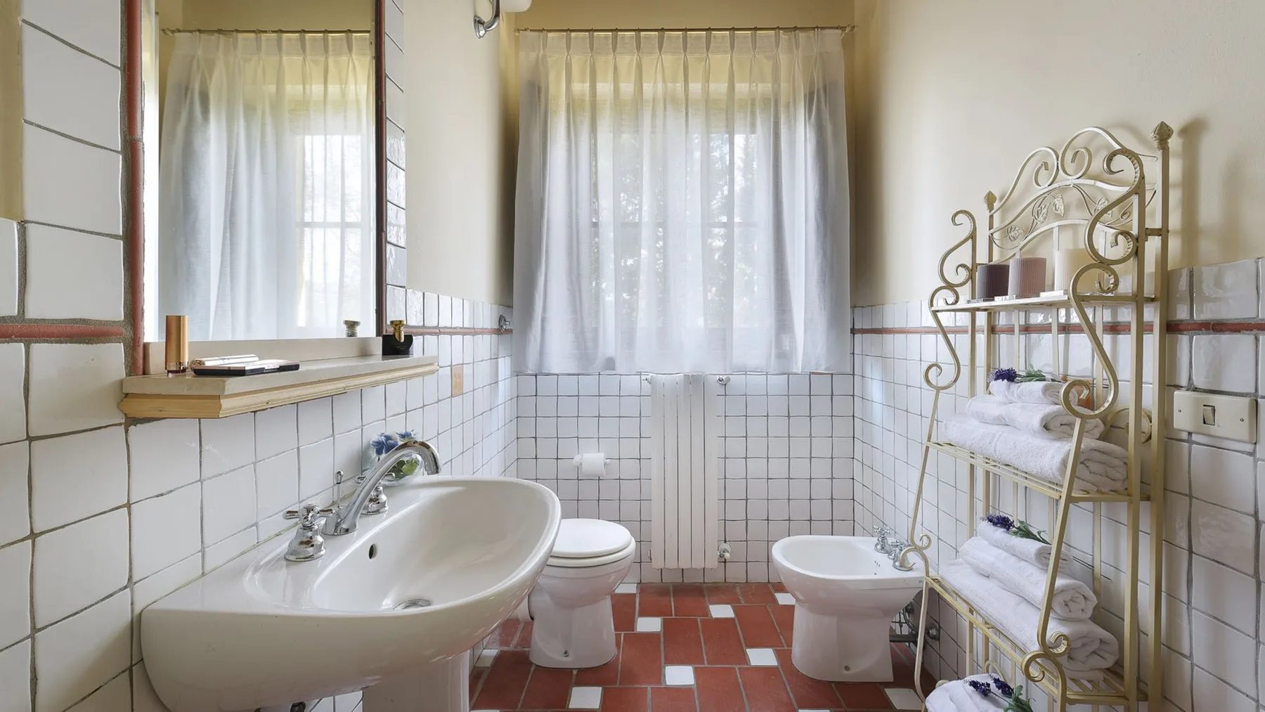 Un baño alicatado con lavabo, inodoro, bidé y ventanas con cortinas.