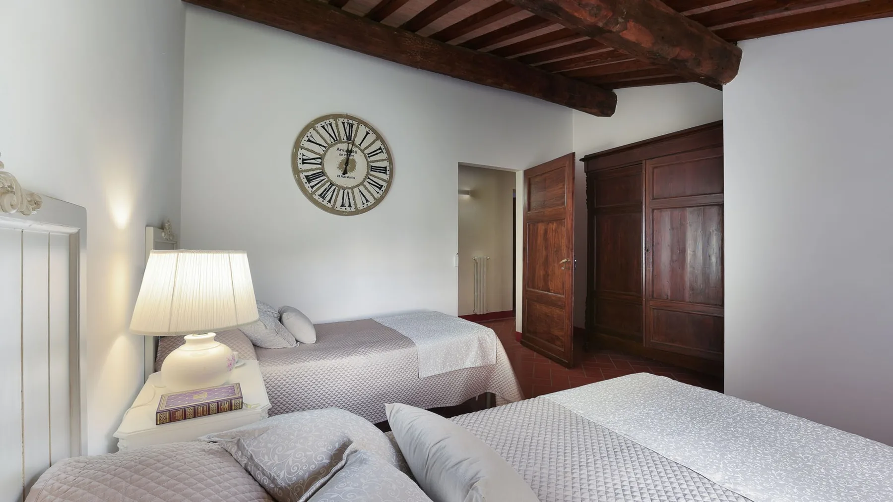 Un dormitorio con dos camas, un reloj de pared y vigas de madera expuestas en el techo.