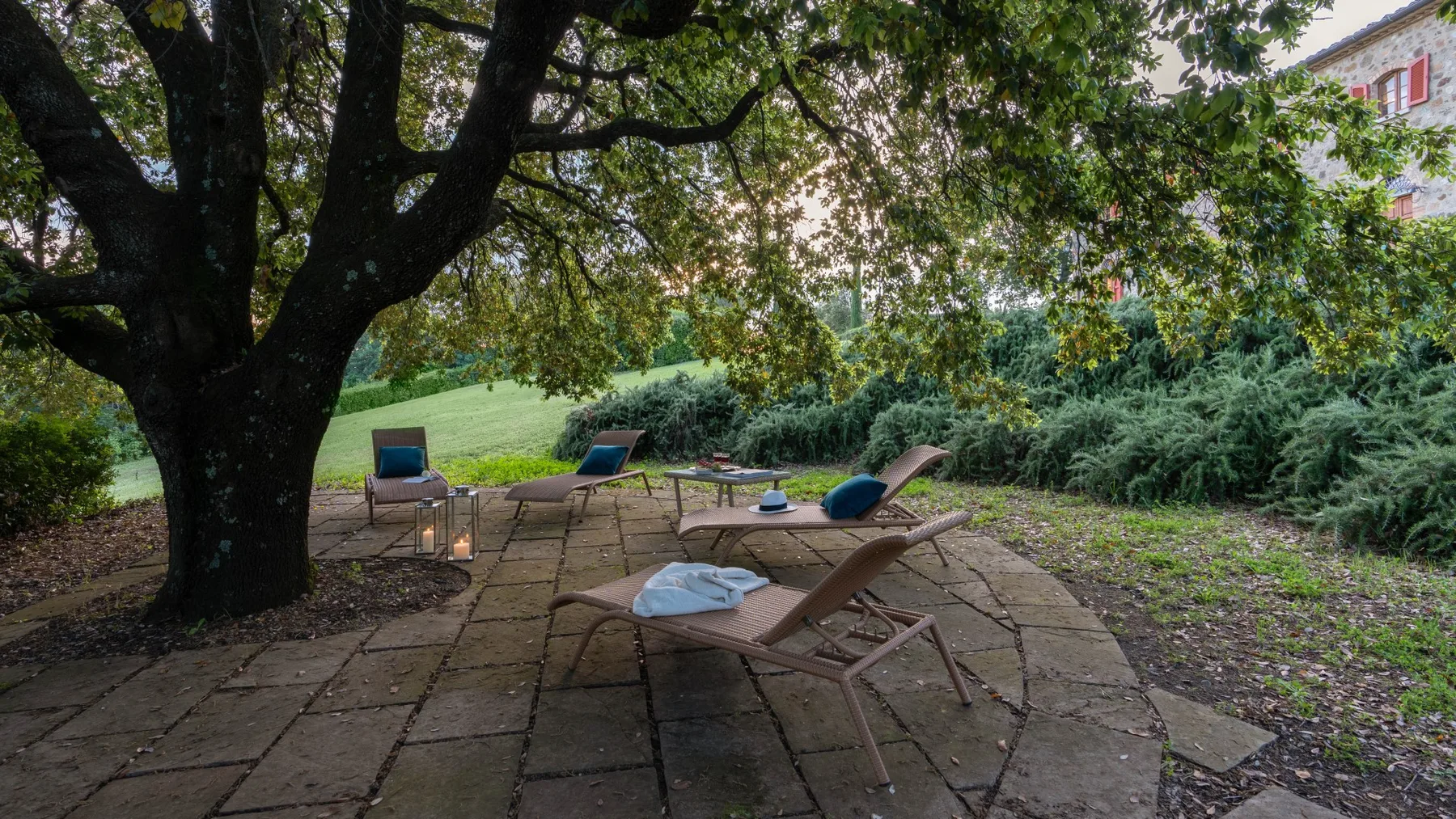 A shaded outdoor patio with reclining seating beneath a large tree.