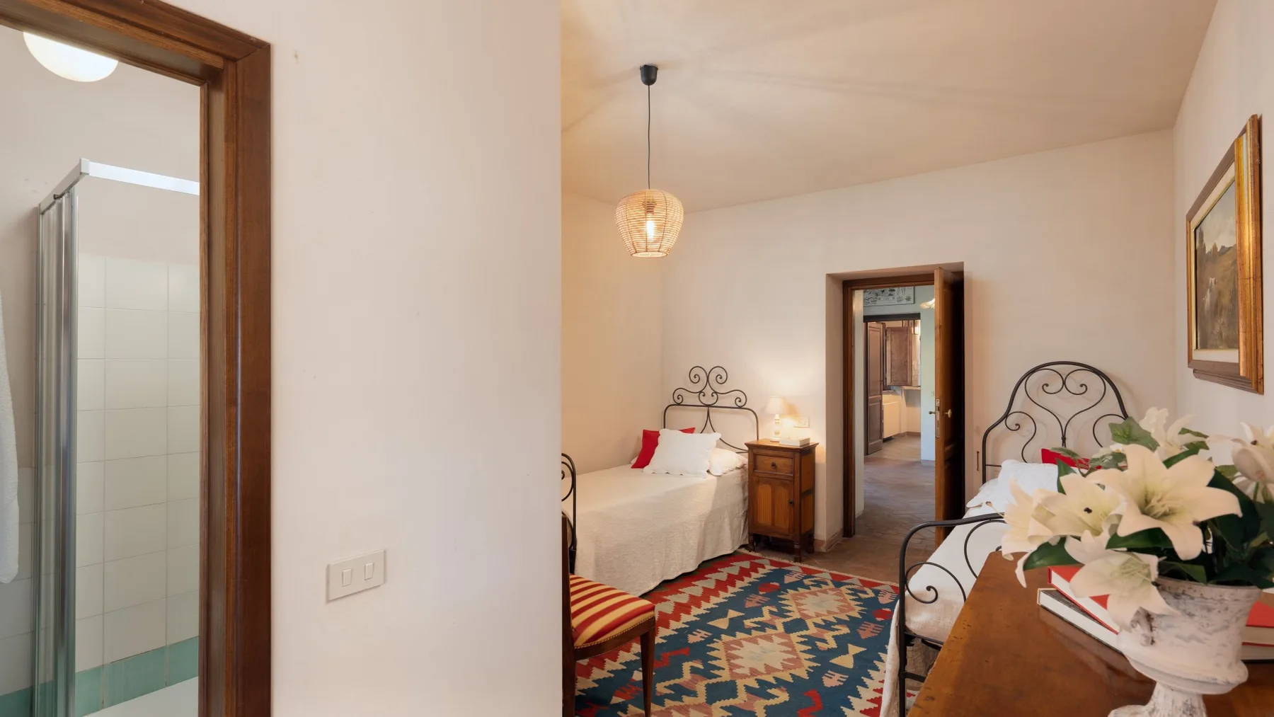 A bedroom with twin beds, patterned rugs, and a doorway to the adjoining room.