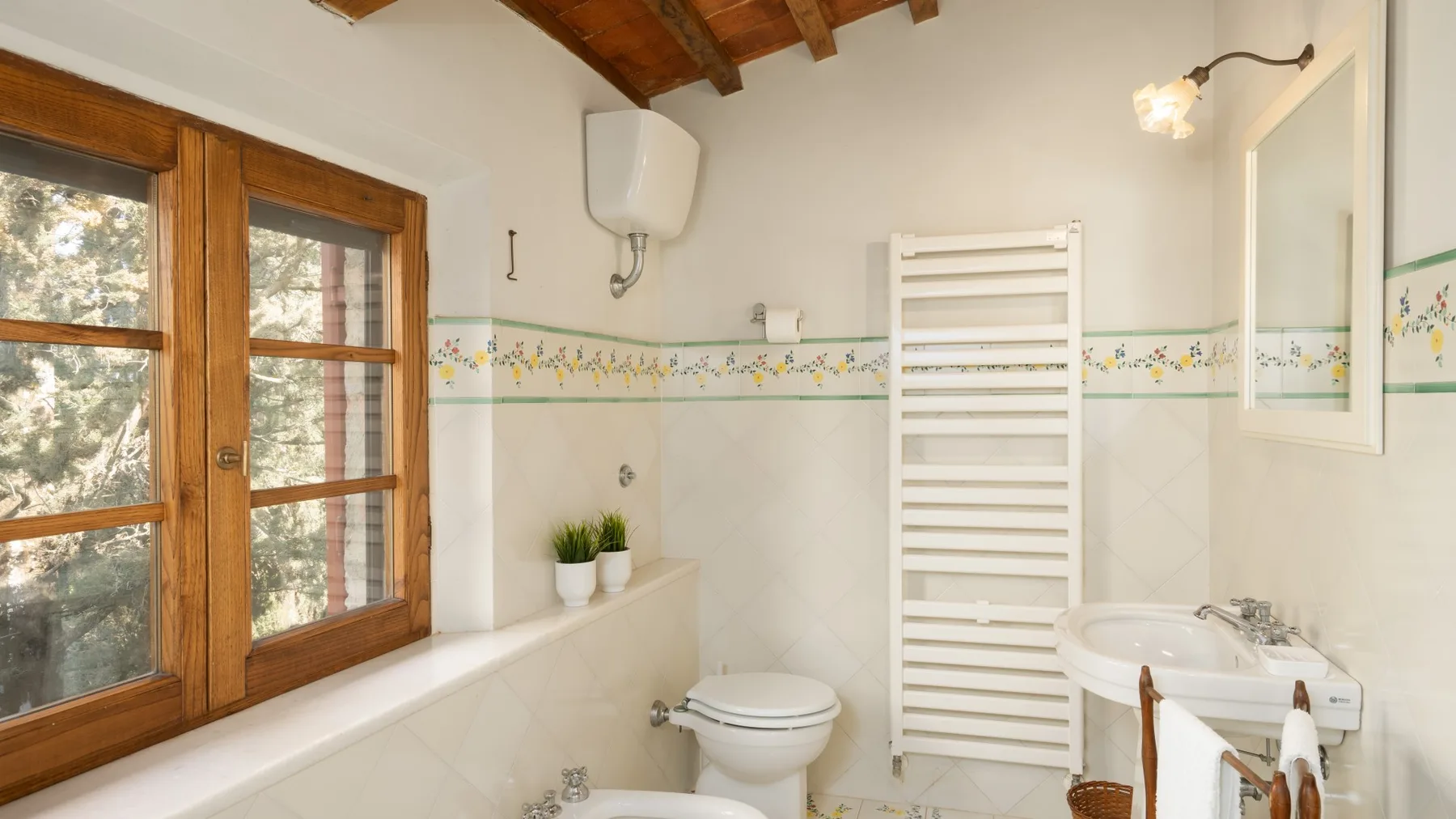 A bathroom with a sink, toilet, and towel warmer beside a wooden-framed window.