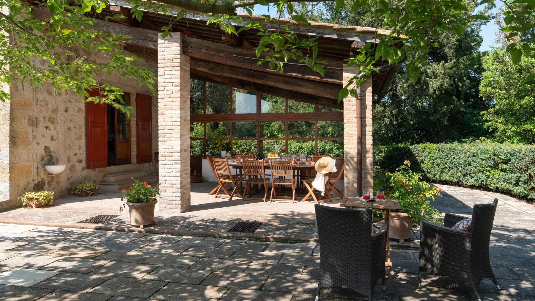 A covered outdoor dining area opens onto a stone-paved patio surrounded by greenery.
