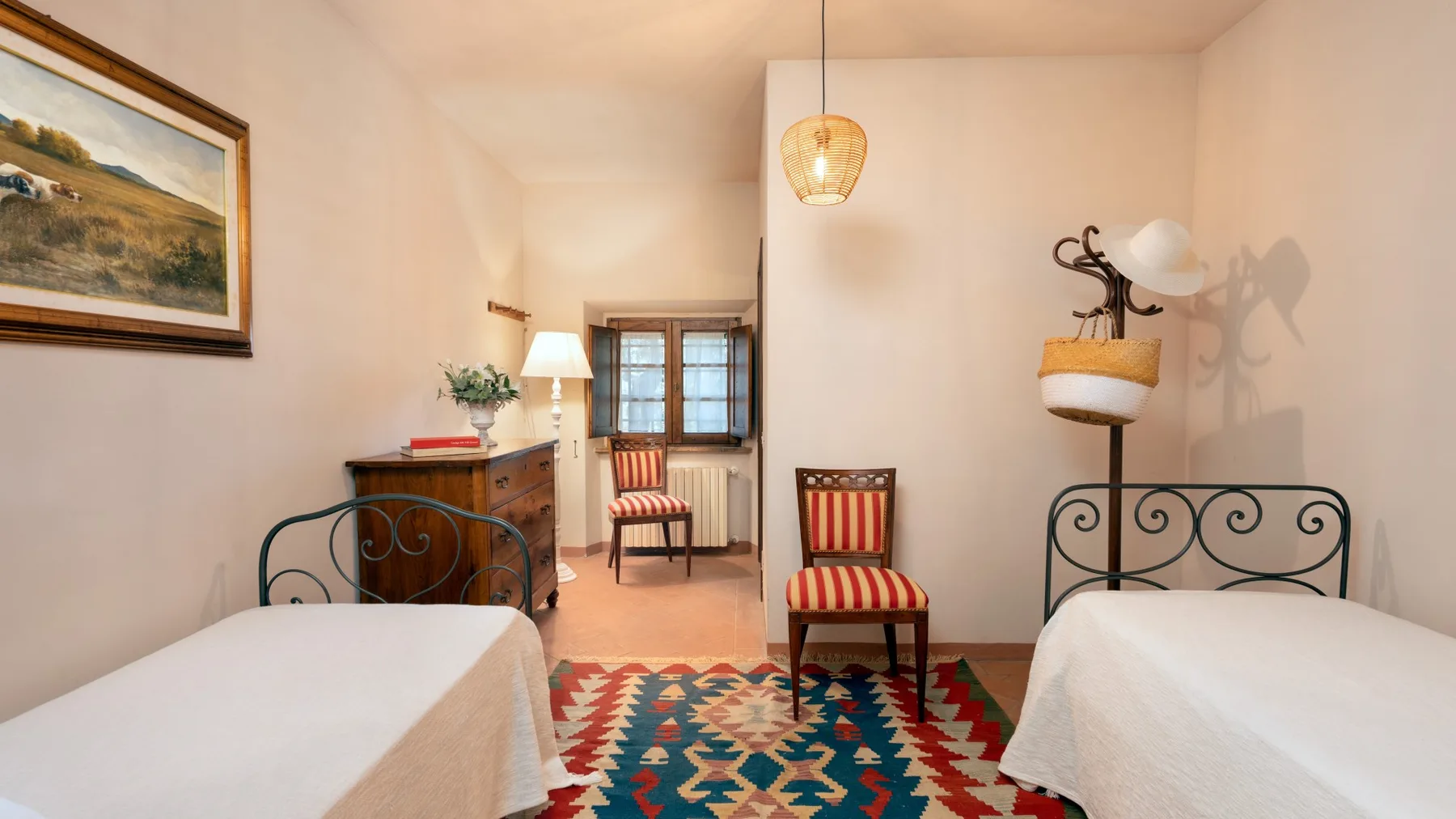 A bedroom with two beds and striped seating around a patterned rug.