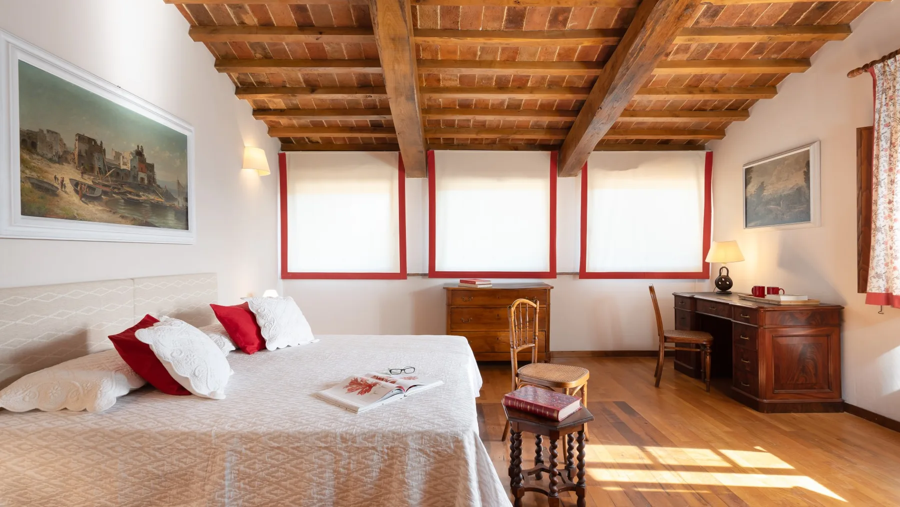A bedroom with a bed, wooden ceiling beams, and a writing desk.