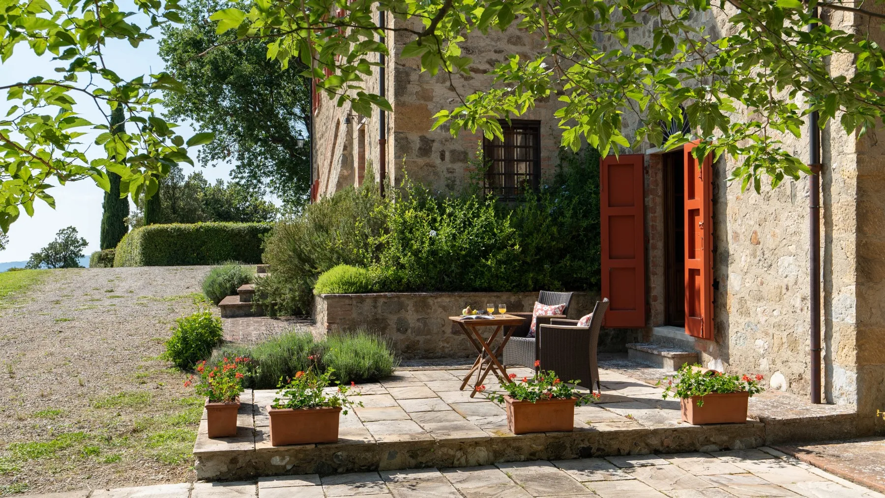 A stone patio beside a building has outdoor seating and potted plants.