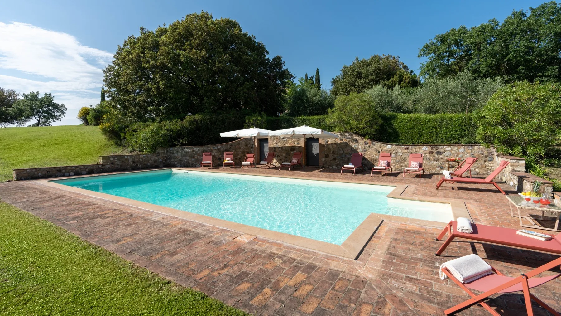 A swimming pool sits beside a paved patio with lounge chairs.