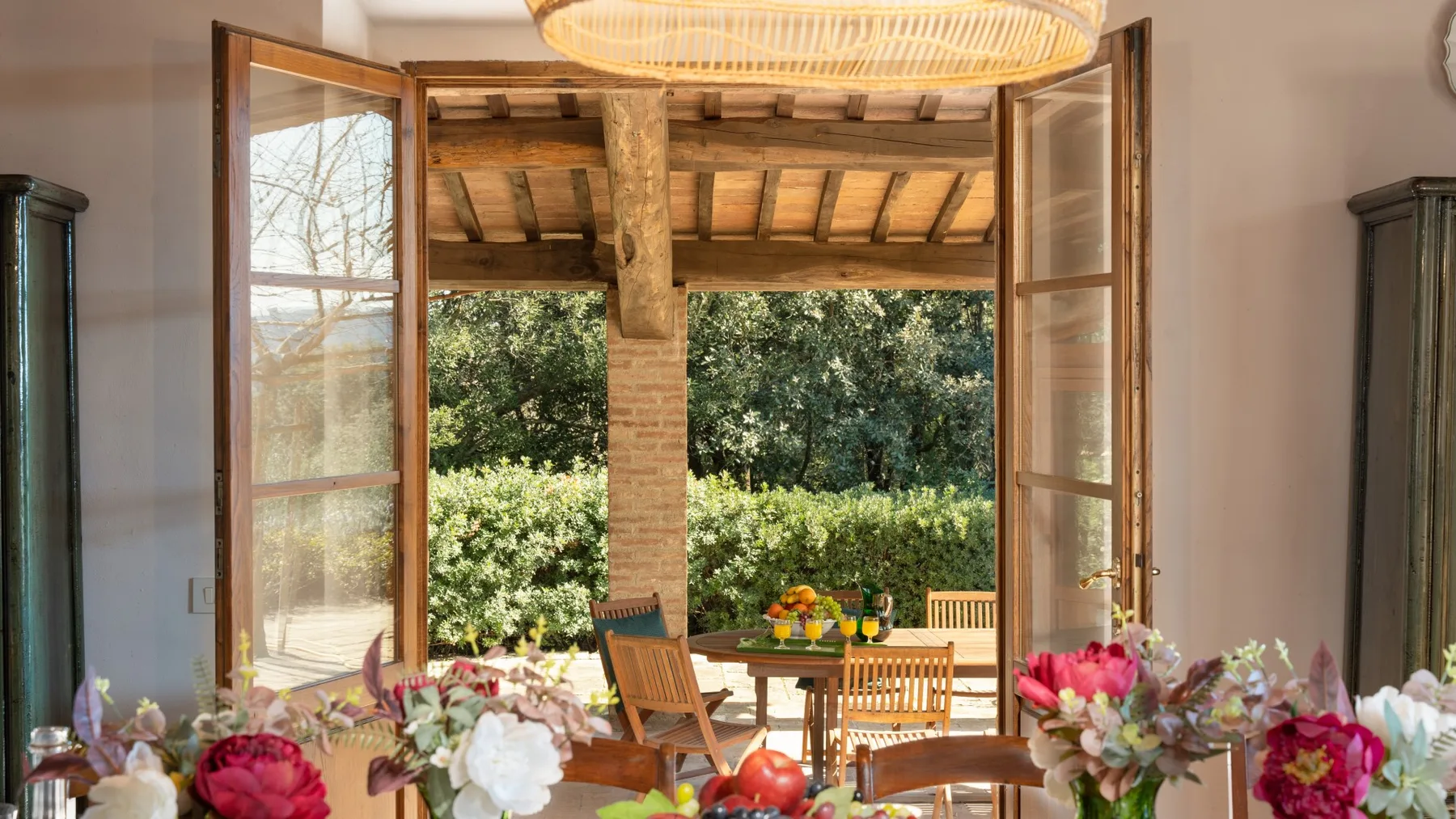 A dining area opens onto a leafy garden through wide wooden doors.