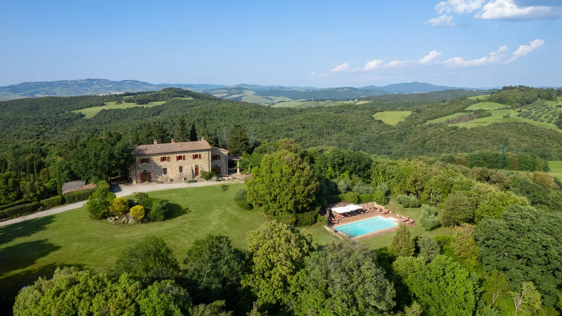 A stone house and outdoor swimming pool sit among green hills and woodland.