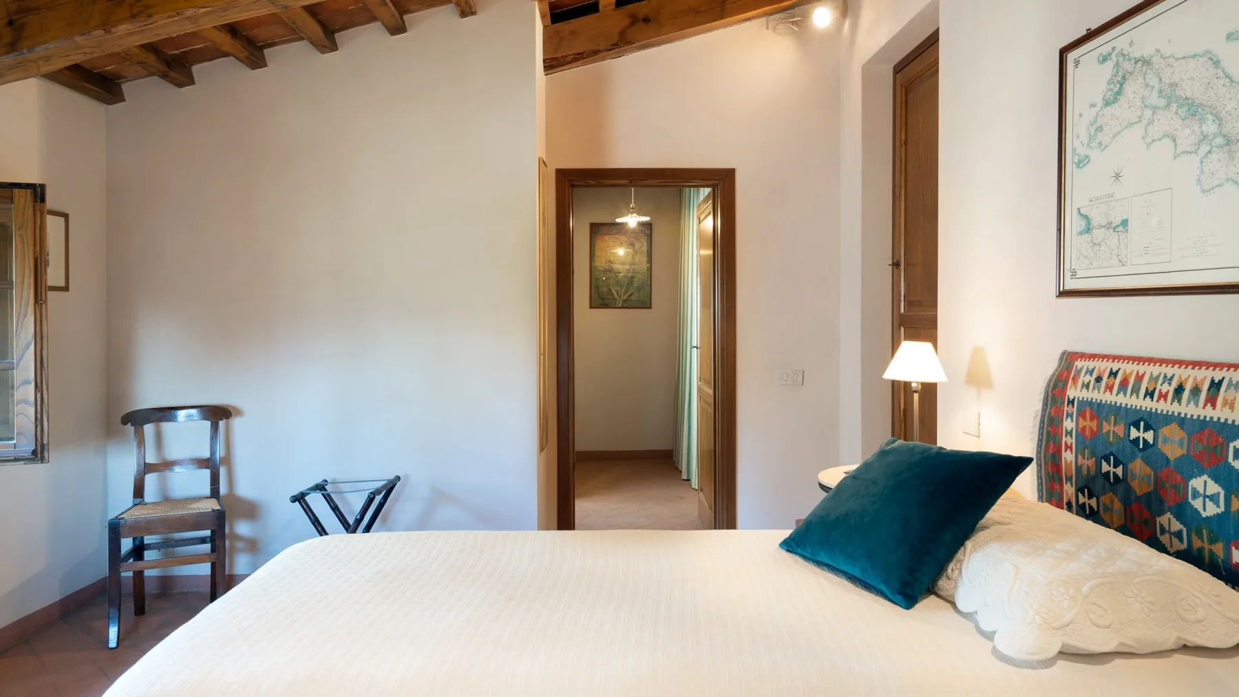A bedroom with a white bed, teal pillow, and wooden ceiling beams.
