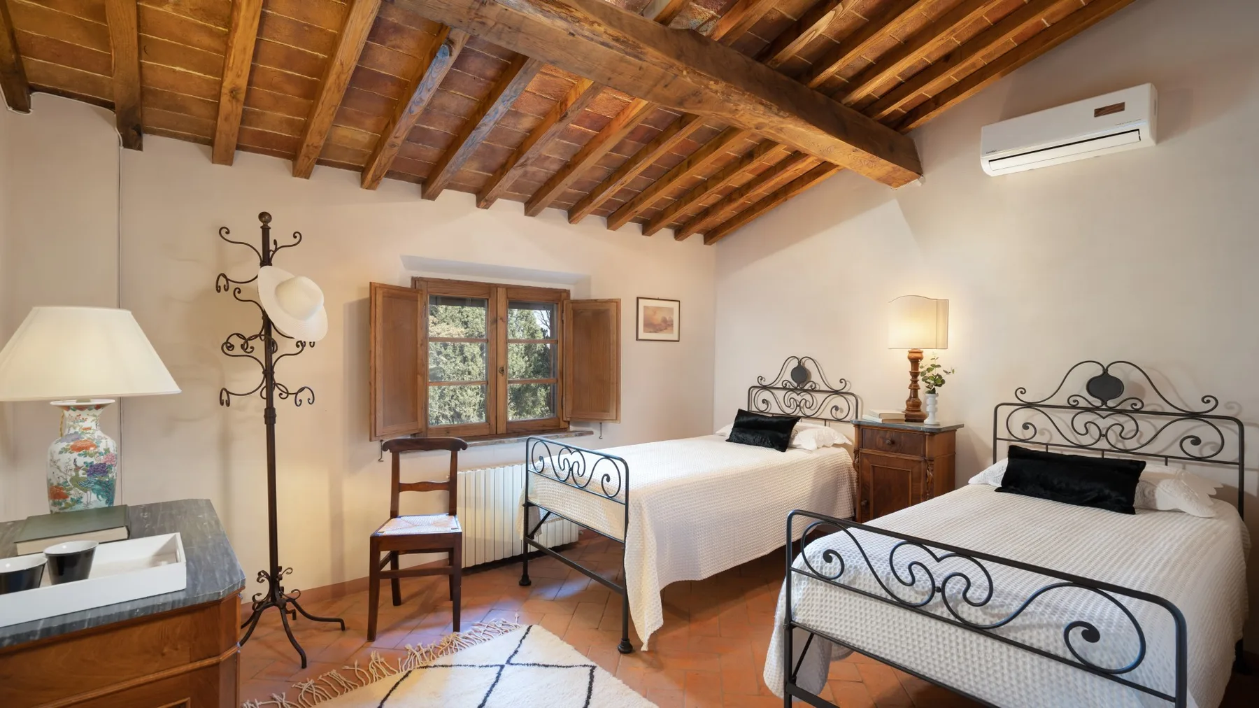 A bedroom with two beds, wooden ceiling beams, and a window.