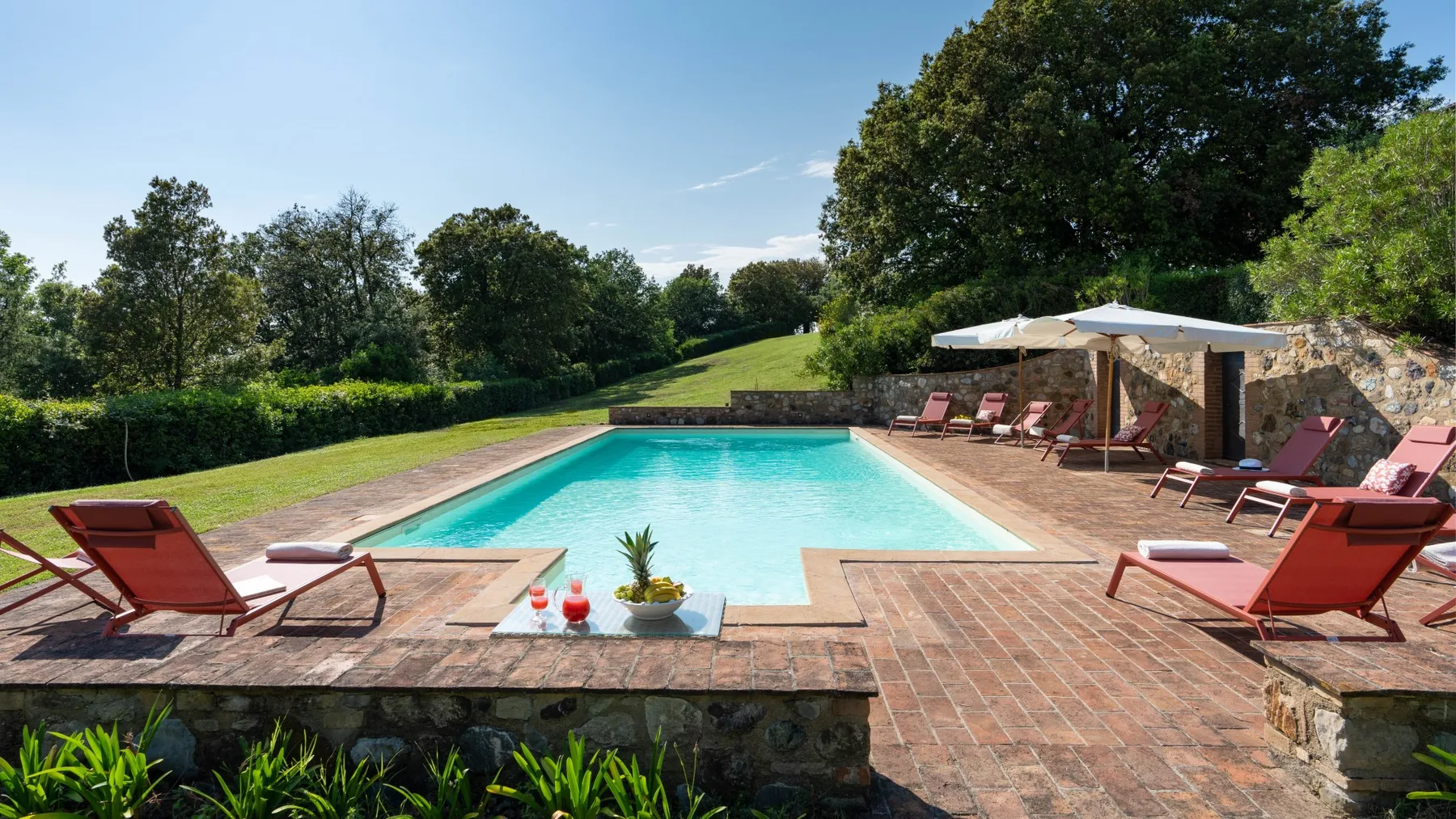 A swimming pool bordered by a brick patio and lounge seating.