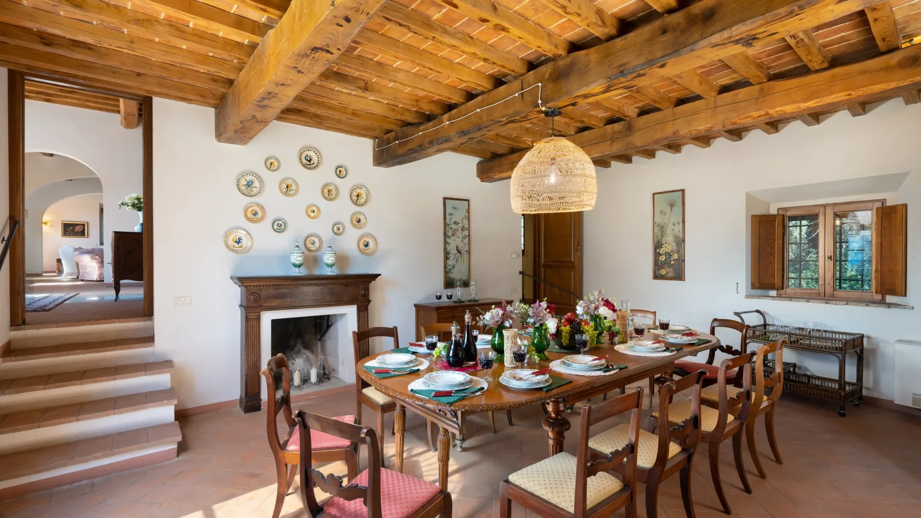 A dining room with a long wooden table set beneath exposed ceiling beams.