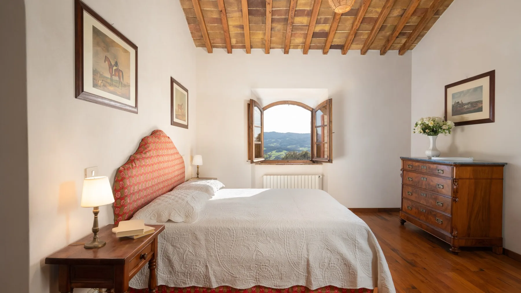 A bedroom with a bed beneath a wooden-beam ceiling and an open window.