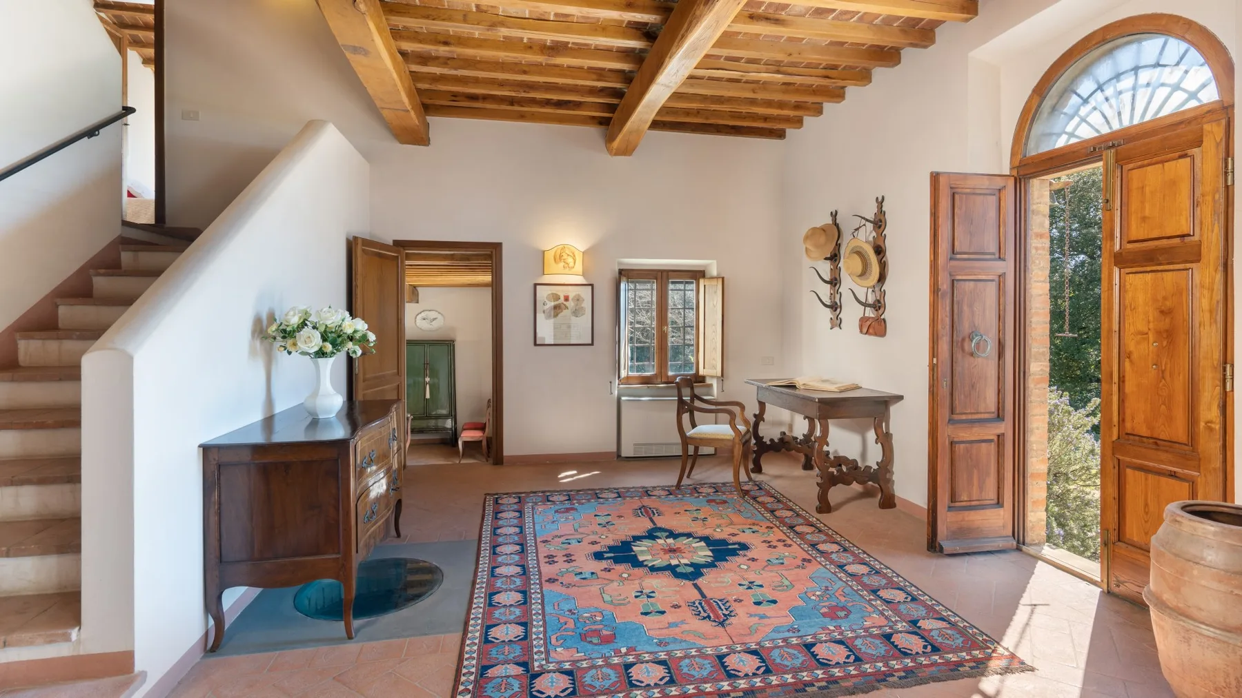 A furnished room with a patterned rug, wooden furniture, and an open doorway.