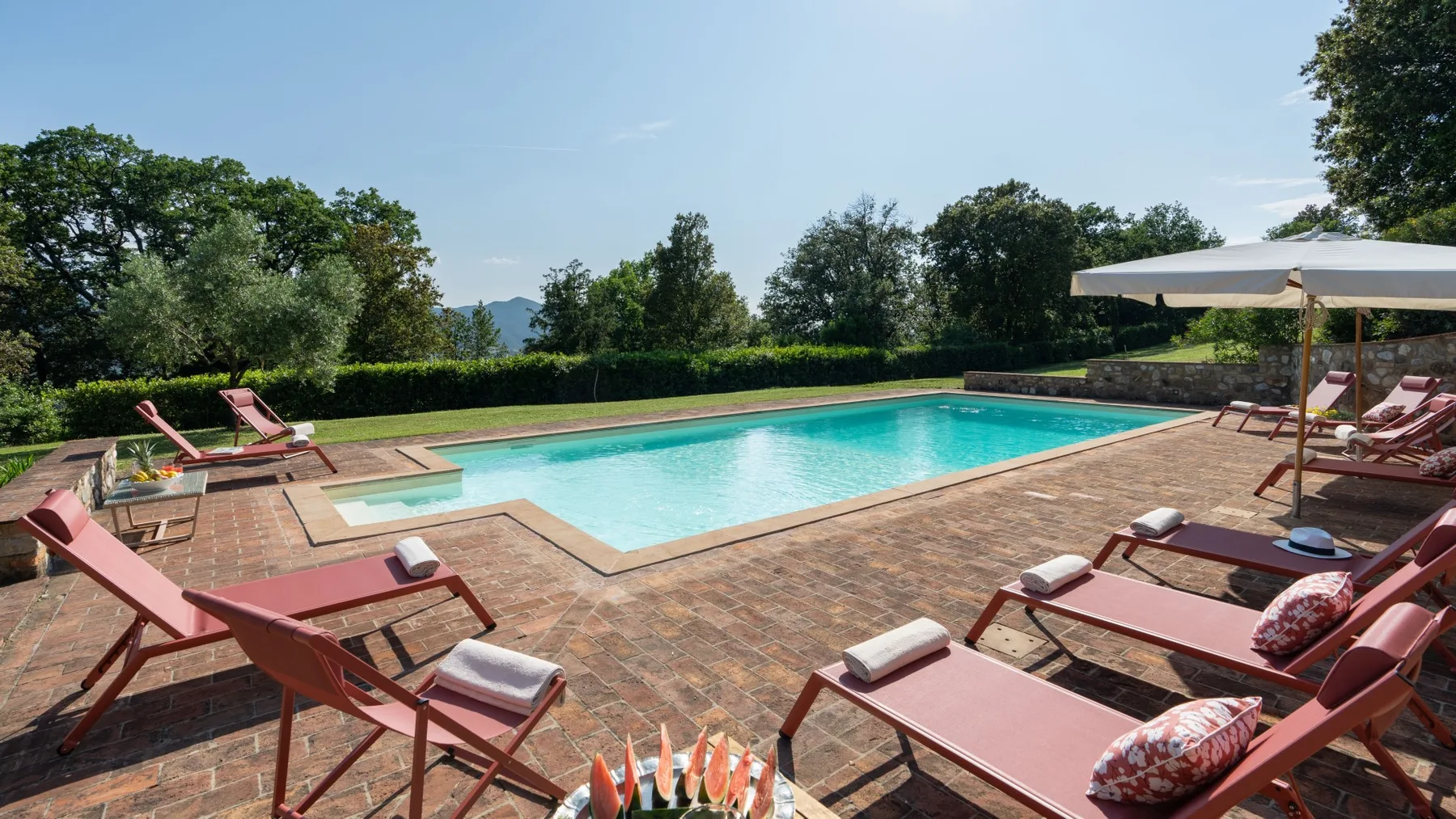 An outdoor swimming pool is surrounded by a paved deck and lounge seating.