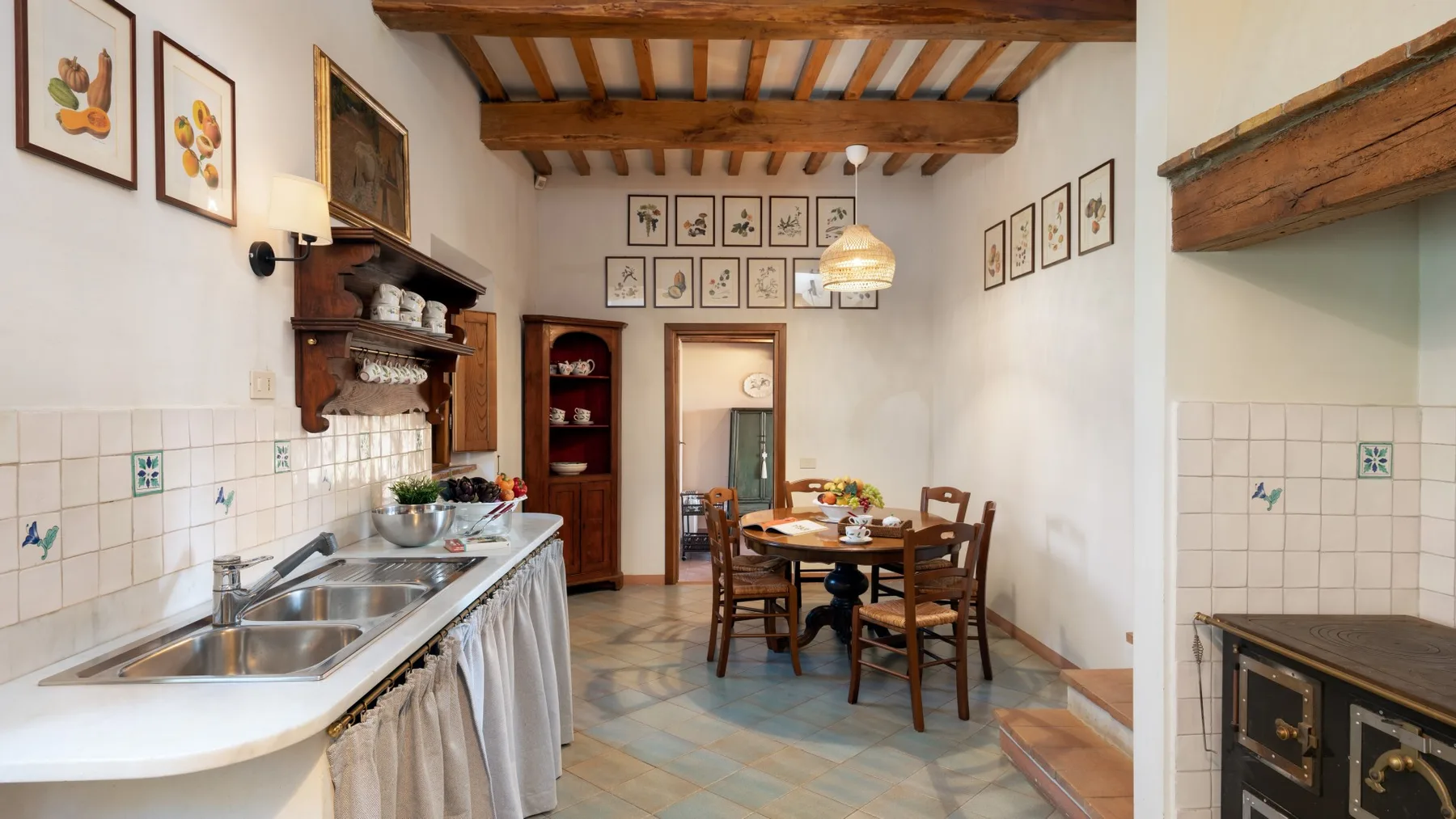 A rustic kitchen with a long counter and a dining table beneath exposed wooden beams.