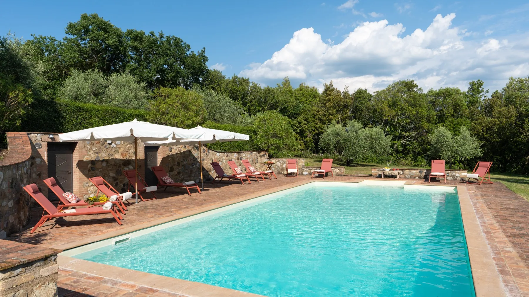 An outdoor swimming pool is surrounded by a paved deck and green trees.