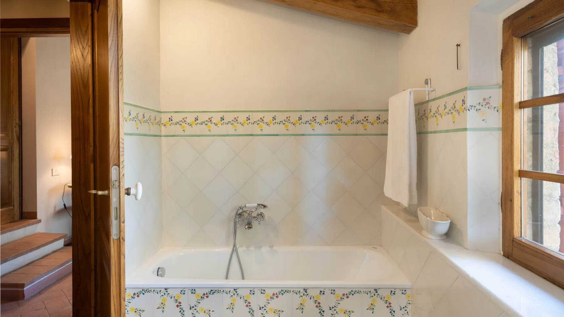A tiled bathroom with a bathtub, shower fixture, and window.