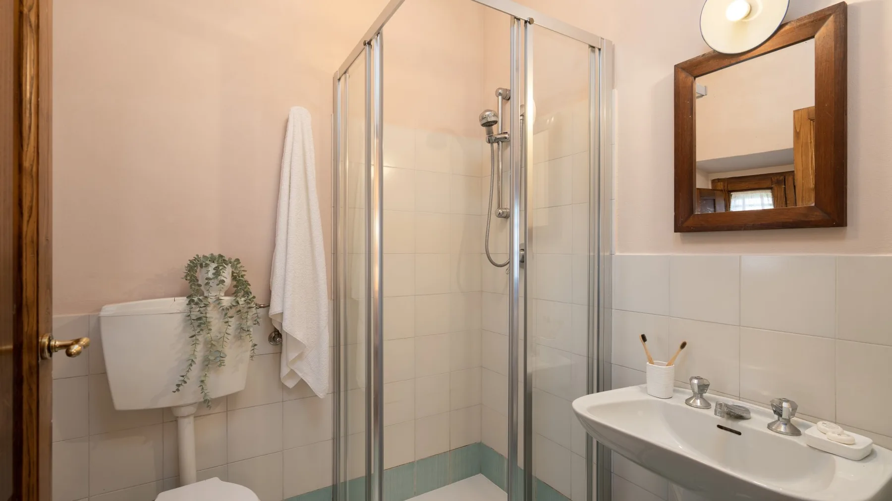 A bathroom with a glass shower, sink, and wall mirror.
