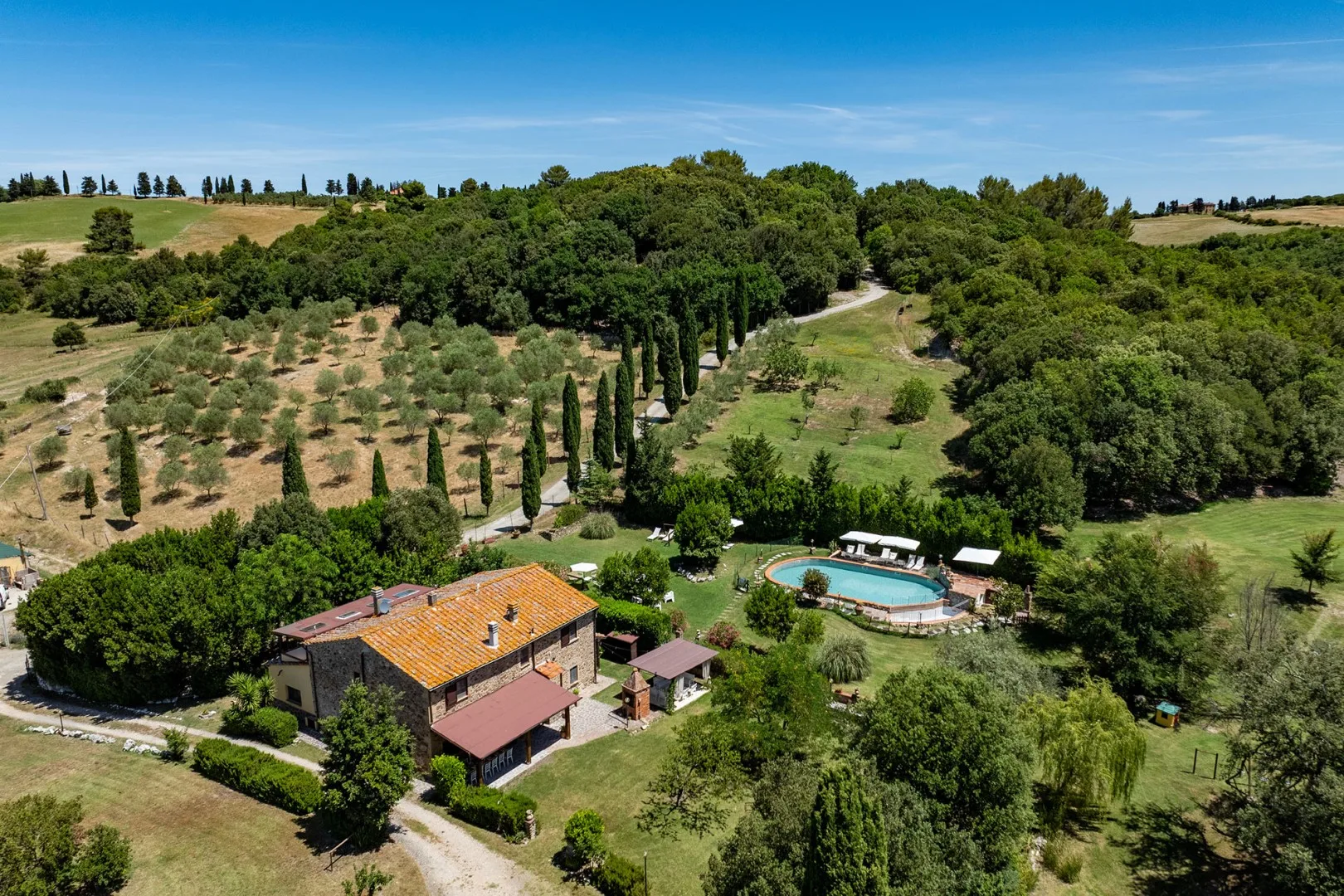 A countryside villa and swimming pool sit among green hills and trees.
