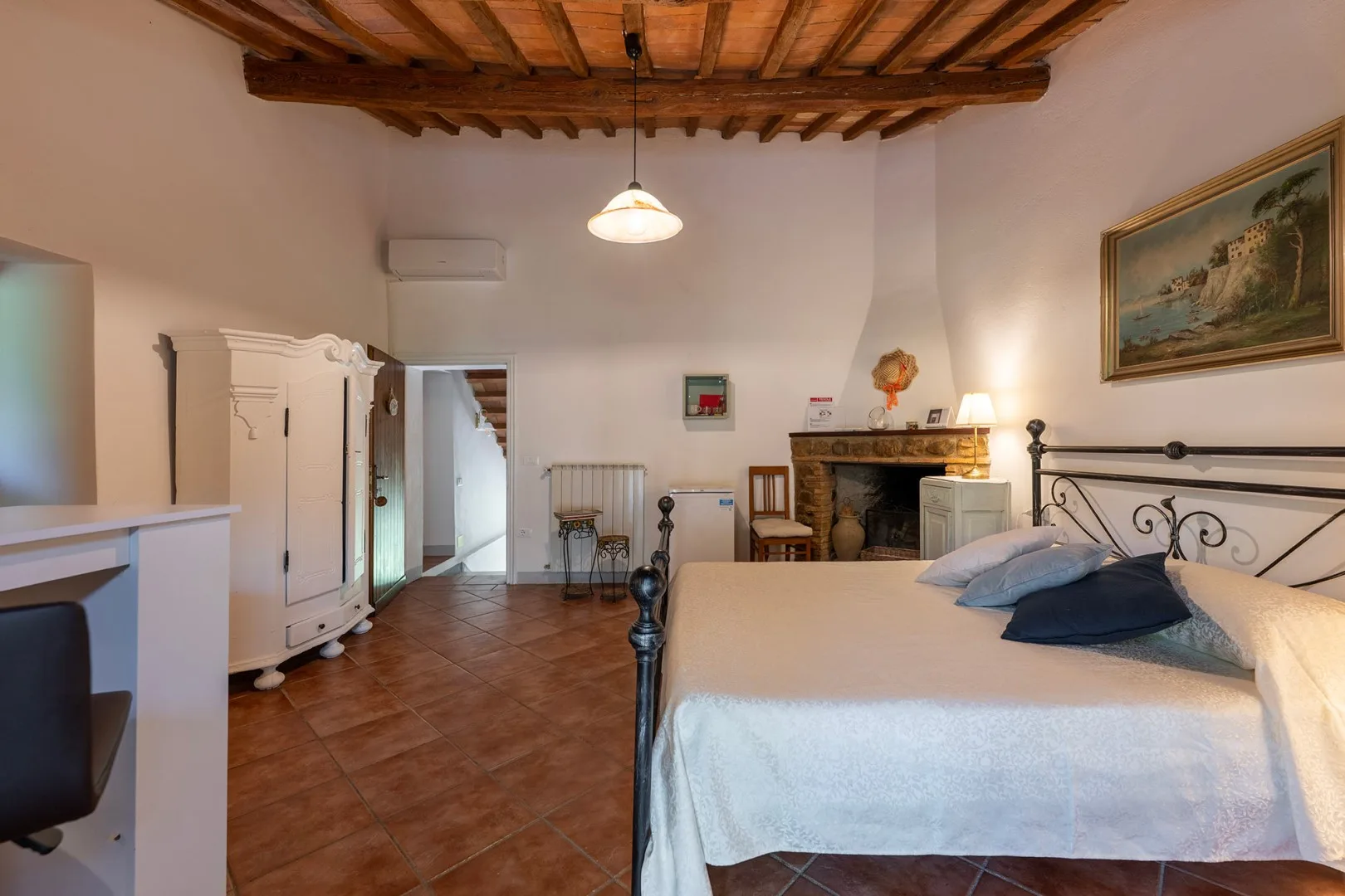 A bedroom with a large bed, tiled floor, and a fireplace.