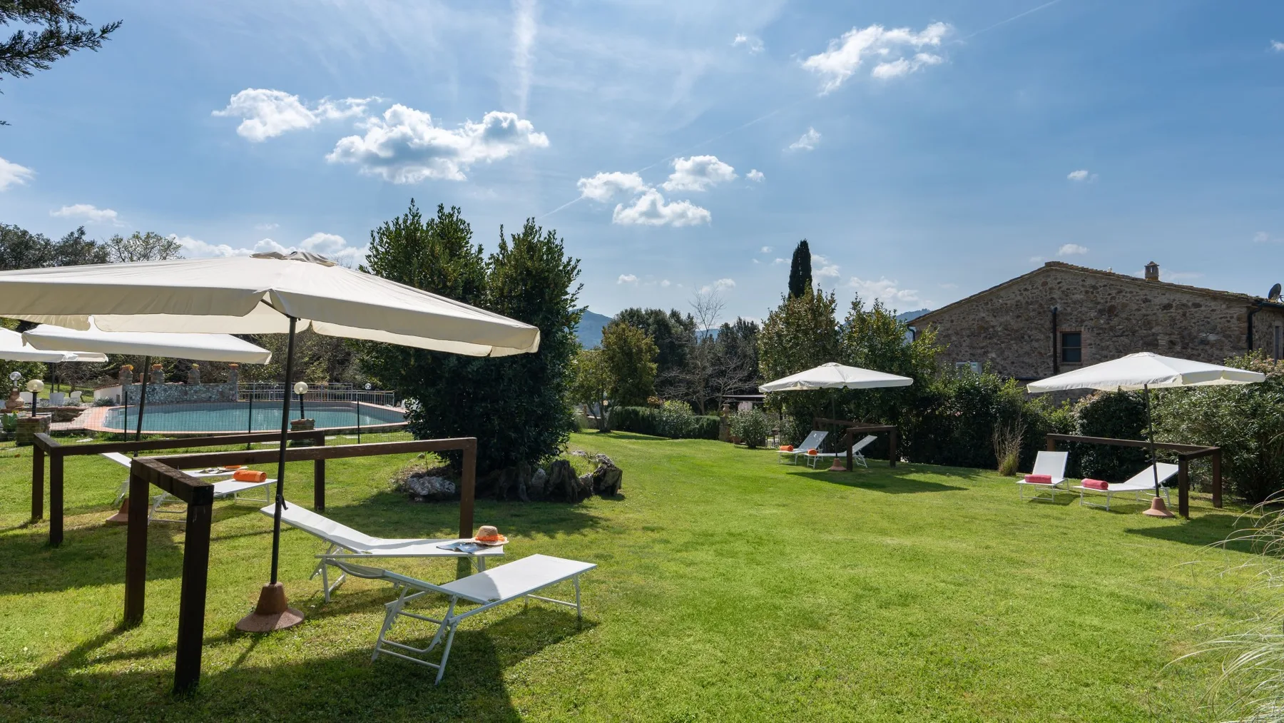 A sunny garden with green lawn, shade umbrellas, and outdoor seating.
