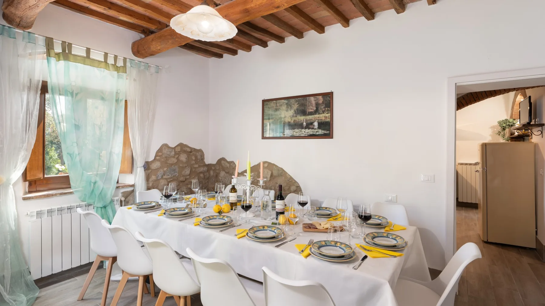 A dining room with a long table set with plates beneath exposed wooden ceiling beams.