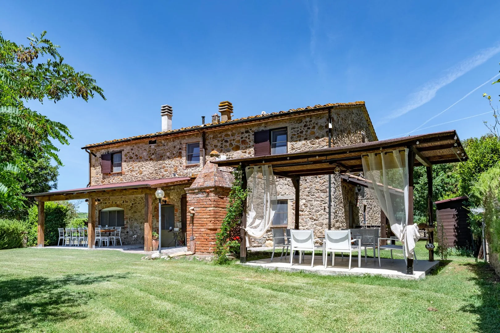 A stone country house with a covered outdoor seating area and grassy yard.