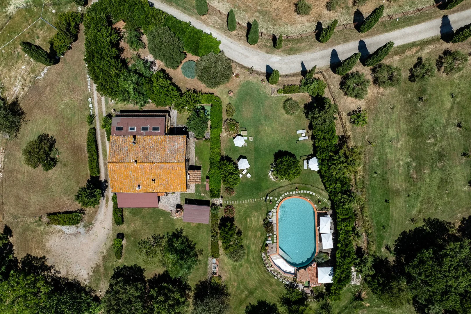 An aerial view of a landscaped property with a tiled-roof building and swimming pool.