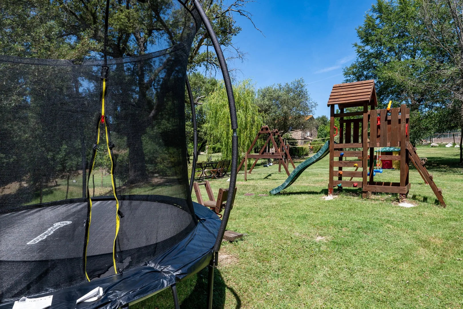 An outdoor play area with a trampoline and a wooden play structure with a slide.