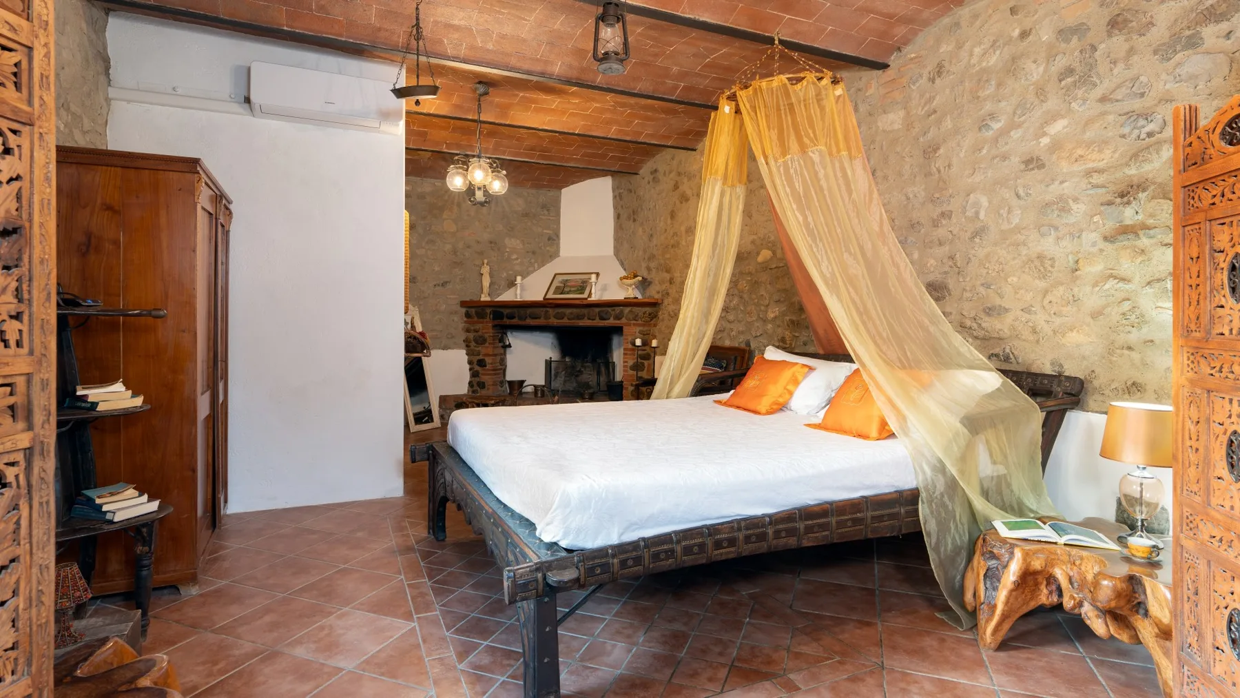 A bedroom with a canopy bed, stone walls, and exposed wooden beams.