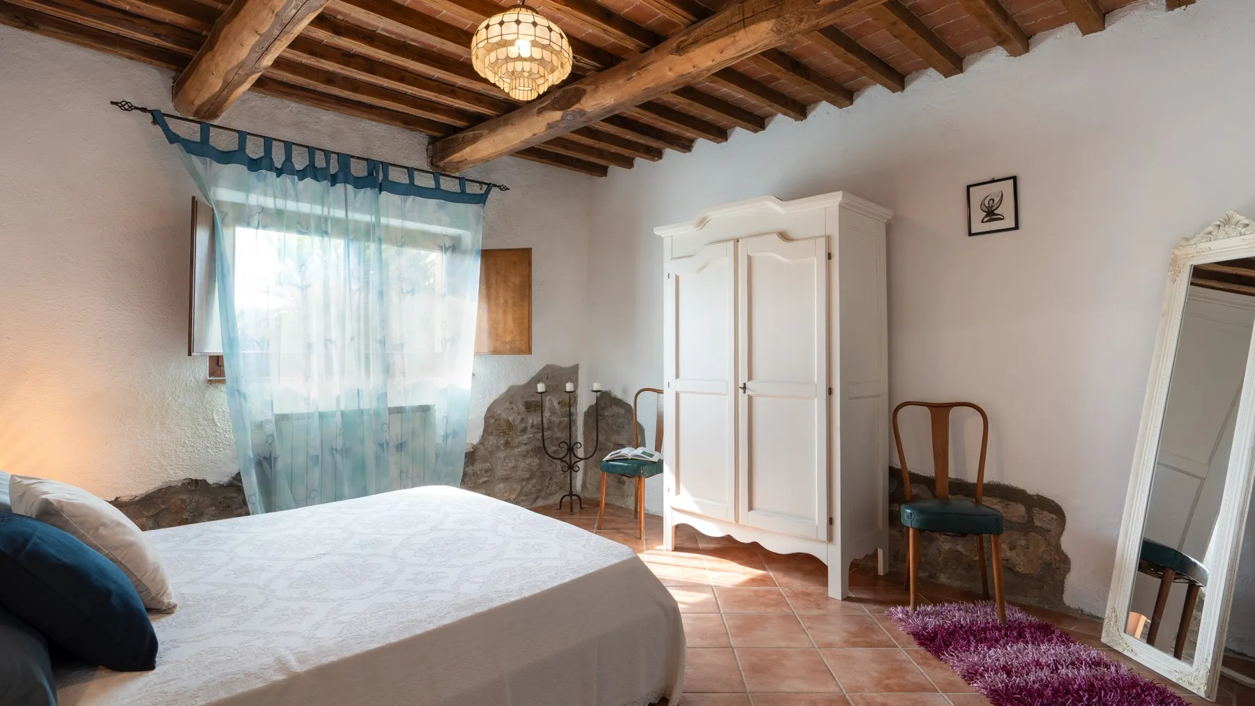 A bedroom with a bed, a wardrobe, and a window covered by sheer curtains.
