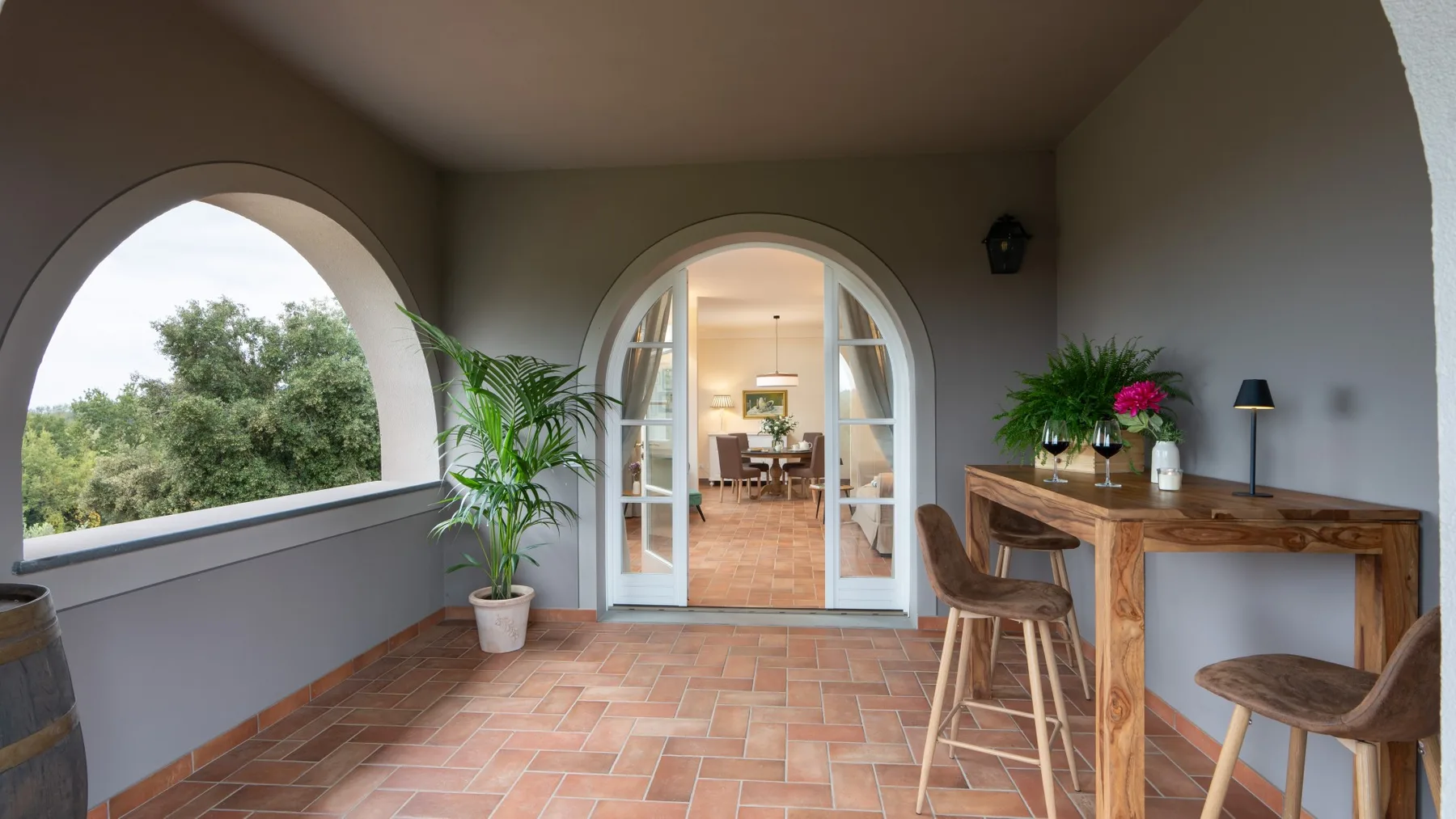 Un patio cubierto se abre a un comedor por puertas arqueadas, con una mesa de madera cerca.