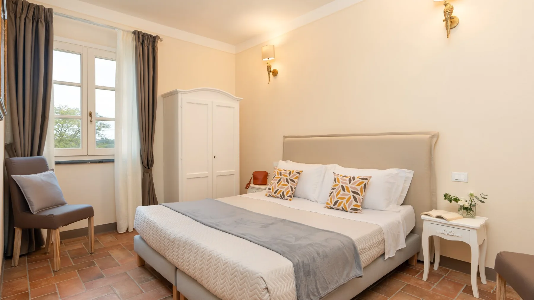 Un dormitorio luminoso con una cama, una ventana con cortinas y un sillón.