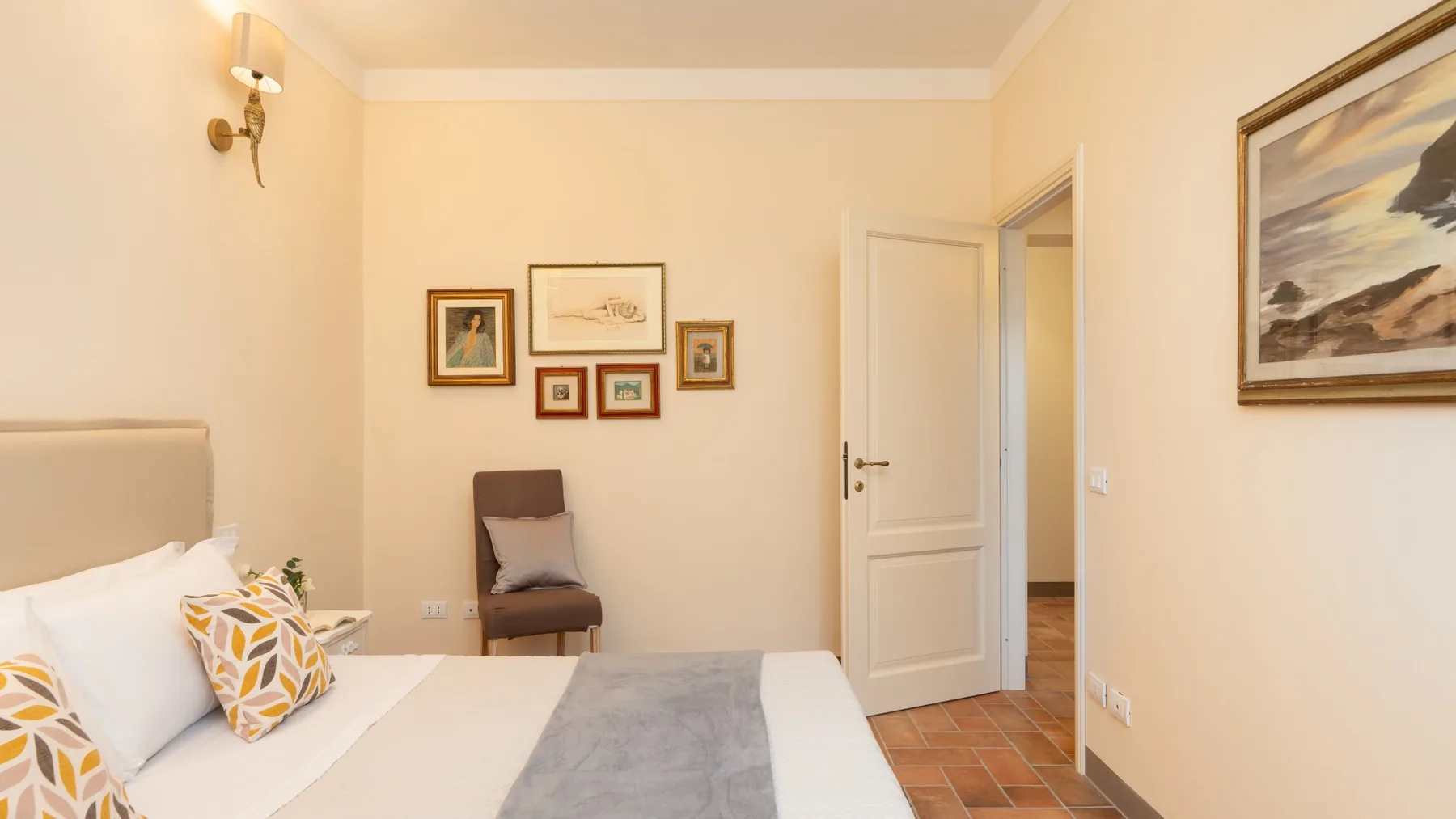 Un dormitorio con una cama, un asiento junto a ella y cuadros en las paredes.
