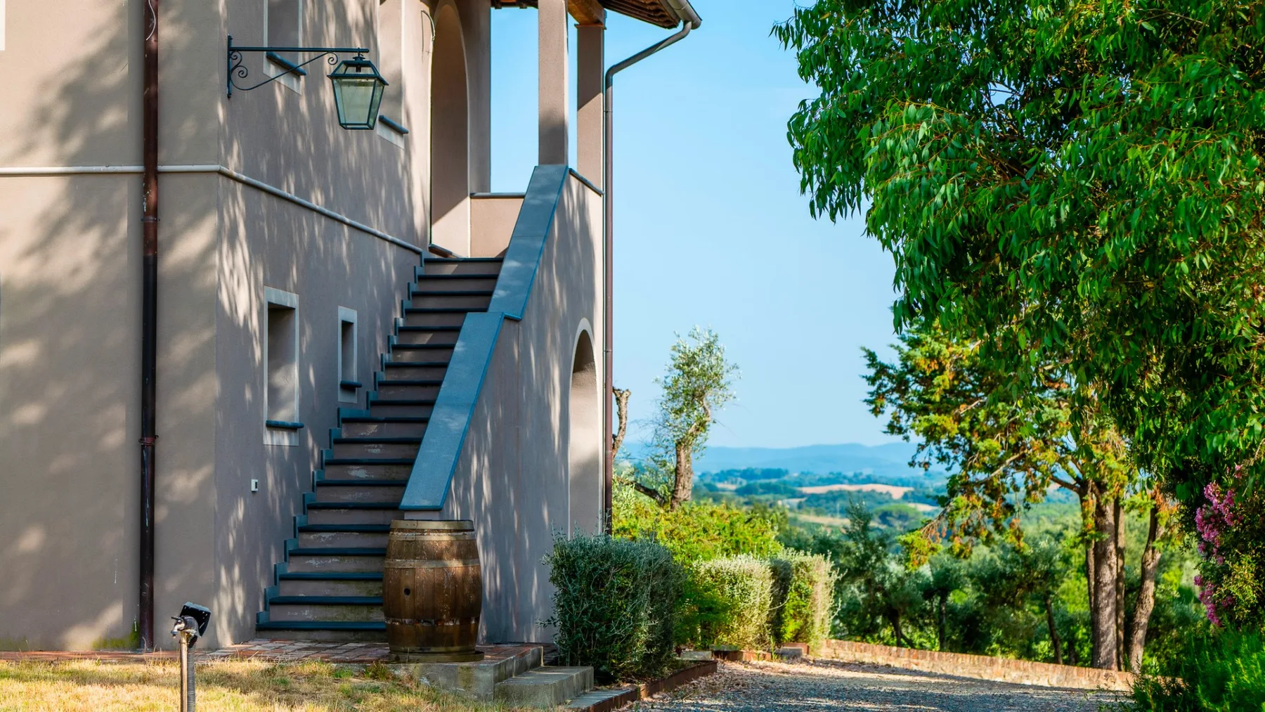 Exterior de un edificio con una escalera al aire libre junto a árboles y un paisaje lejano.