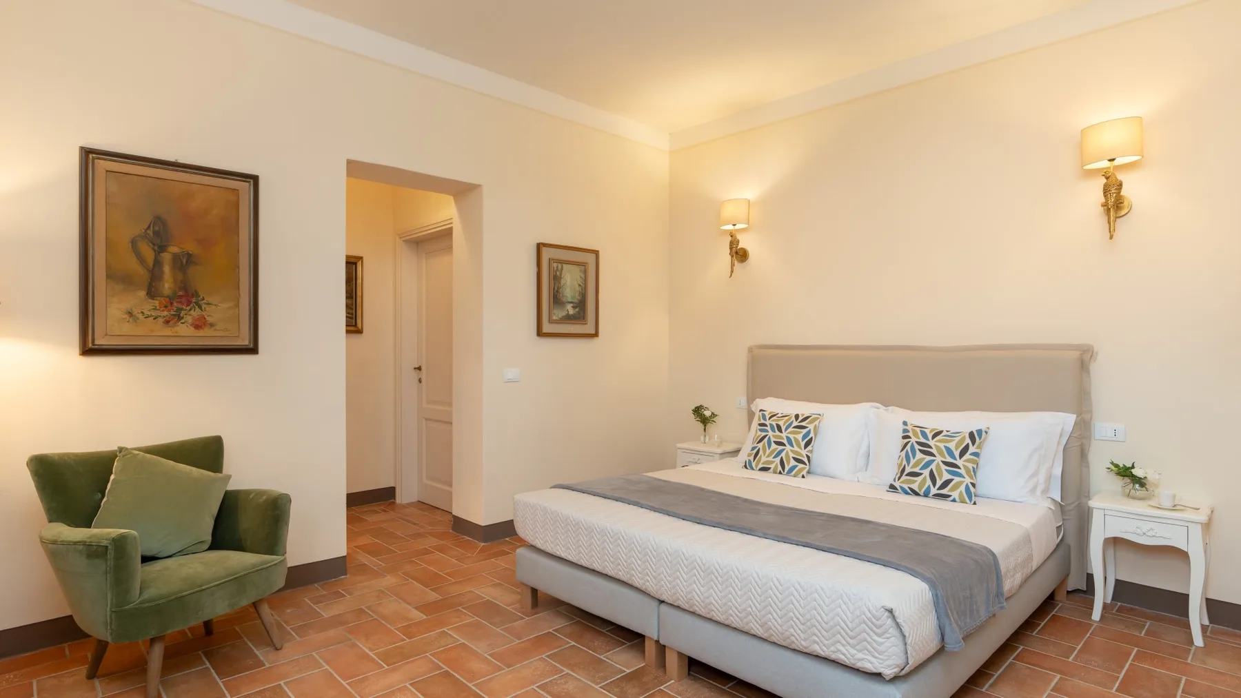 Un dormitorio con una cama grande, un sillón verde y cuadros enmarcados.