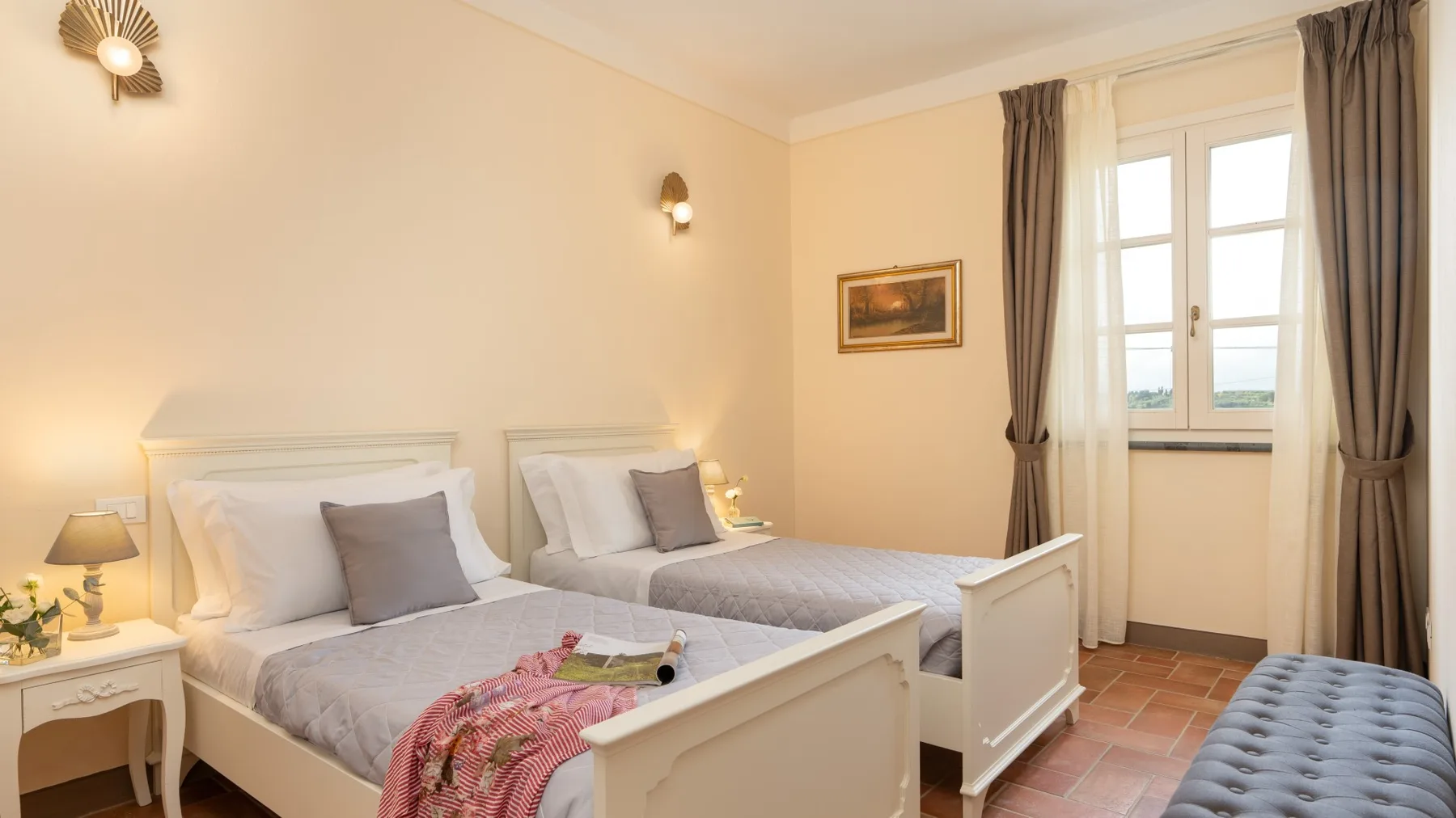 Un dormitorio con dos camas, una ventana y un banco acolchado.
