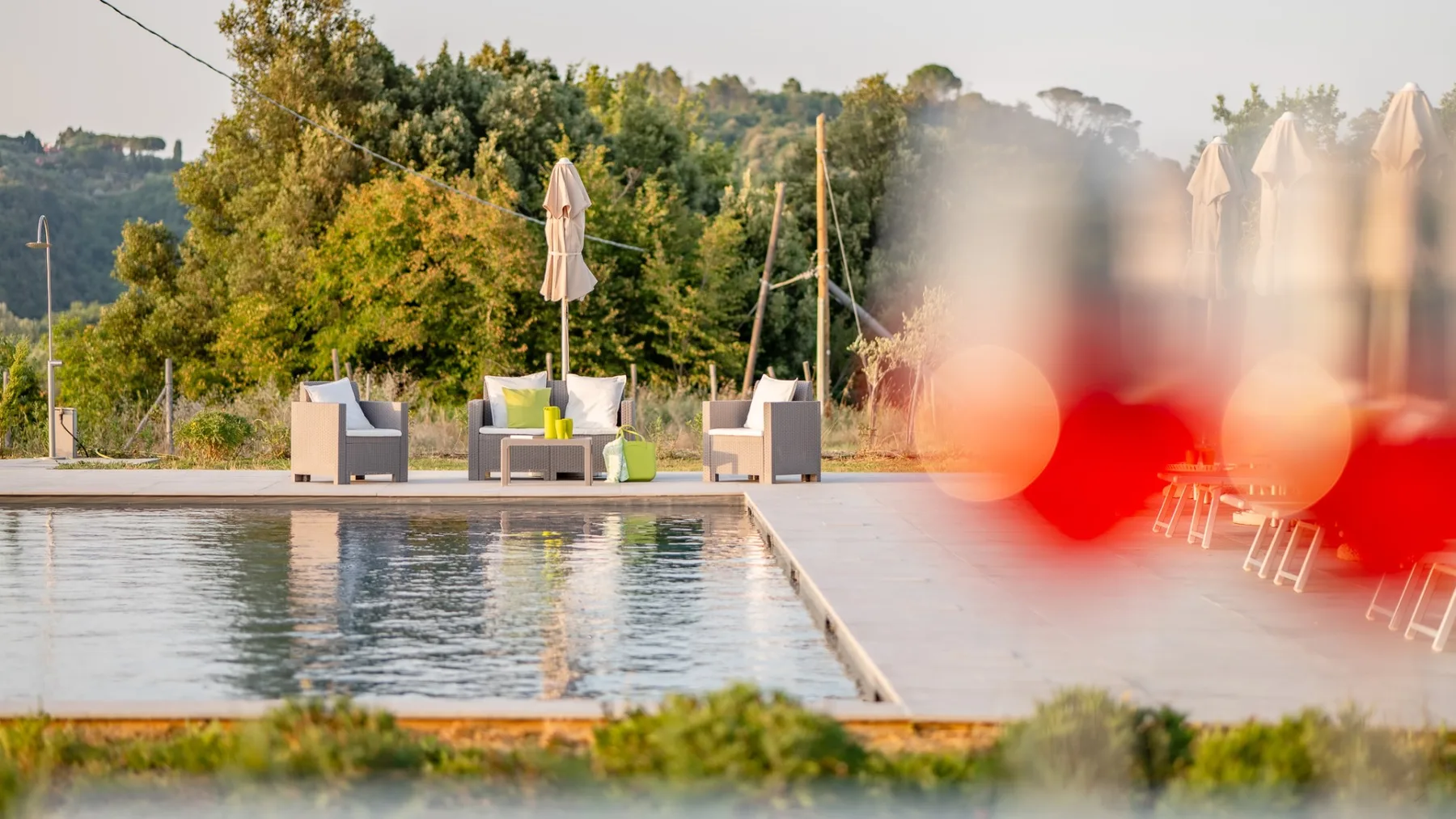 Una piscina al aire libre junto a una zona de asientos, con árboles al fondo.